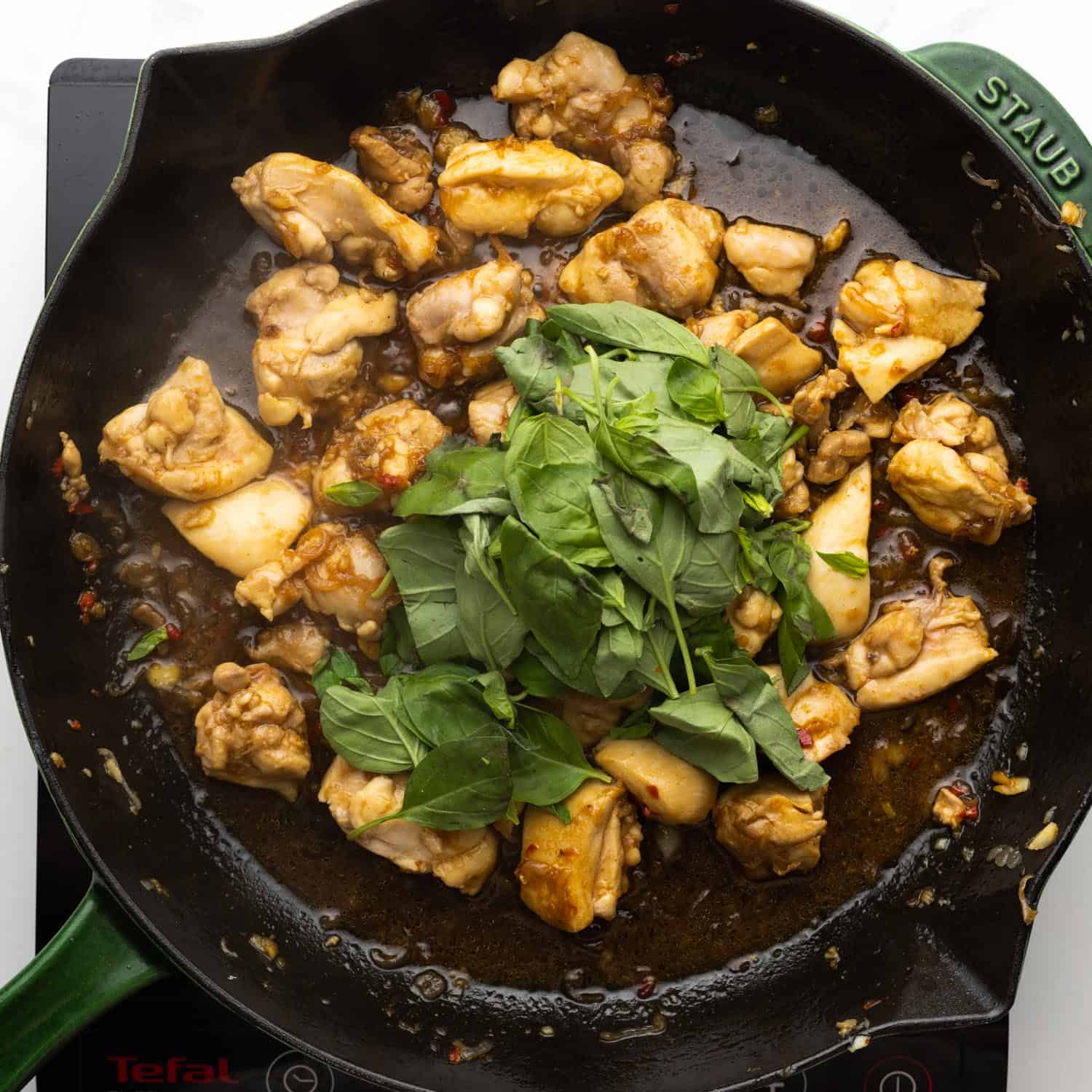 thai basil leaves added to a skillet of cooked chicken to wilt.