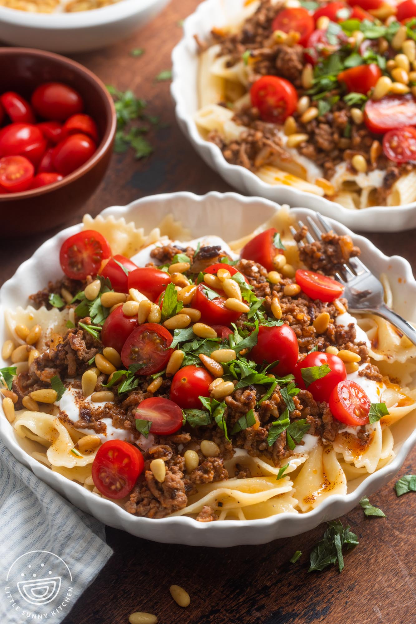 Two bowls of Turkish pasta topped with yogurt, ground beef, tomatoes, pinenuts, and herbs.