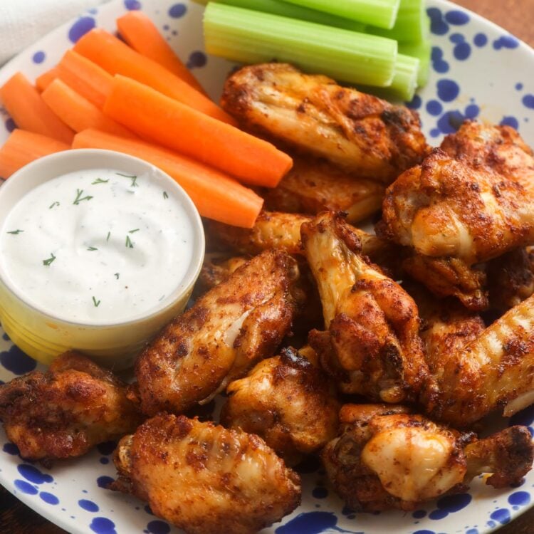 a plate of seasoned air fryer fried chicken wings with a side of ranch, carrot sticks, and celery sticks.