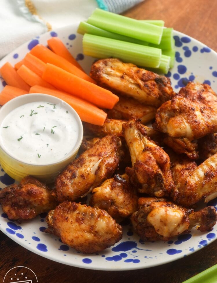 a plate of seasoned air fryer fried chicken wings with a side of ranch, carrot sticks, and celery sticks.