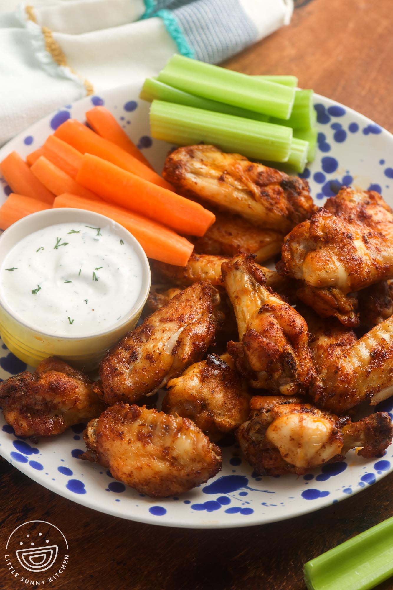 a plate of seasoned air fryer fried chicken wings with a side of ranch, carrot sticks, and celery sticks.