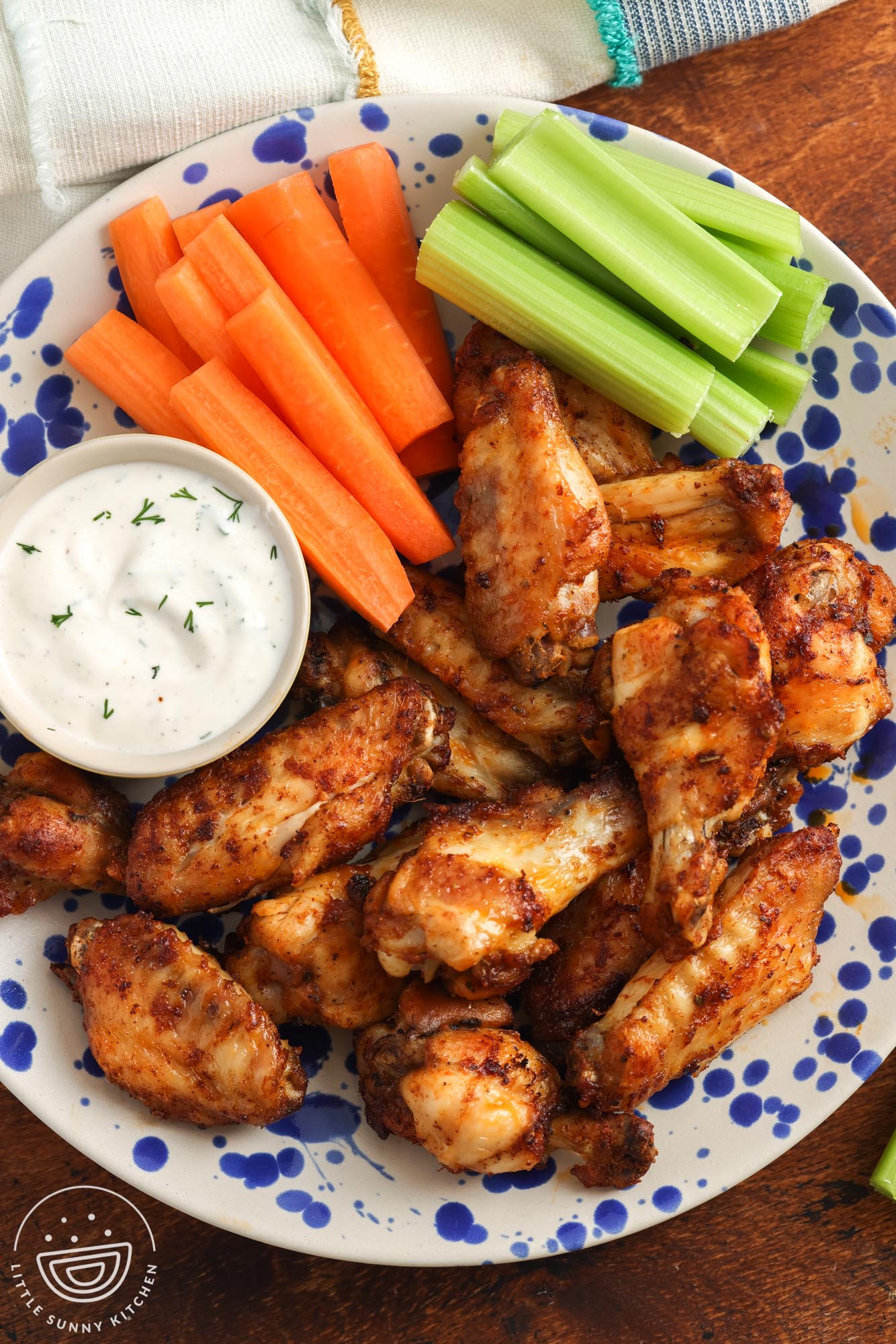 overhead view of a platter of chicken wings in air fryer with a side of creamy dip and veggie sticks.