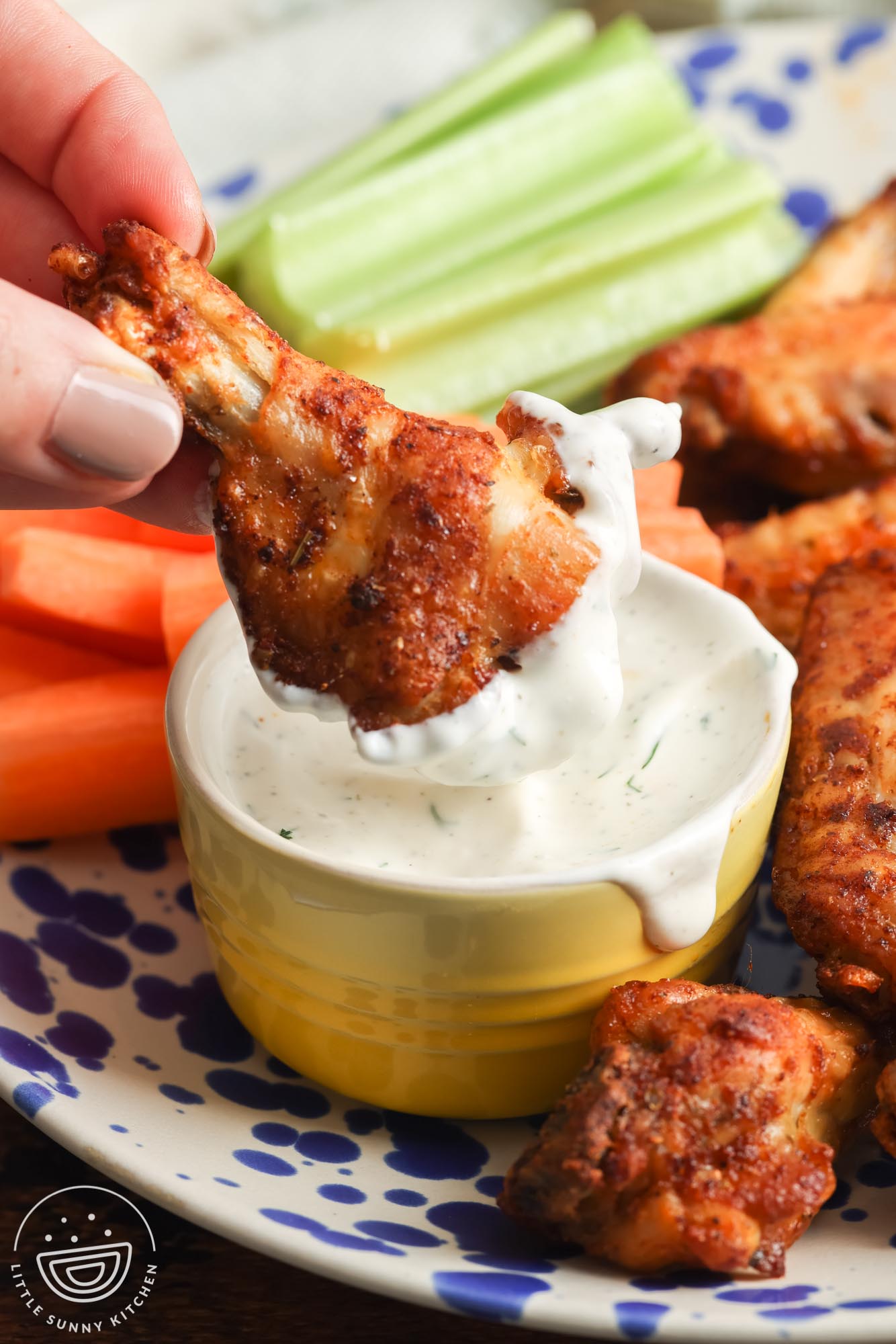 a hand dipping a drum chicken wing into a cup of ranch dressing.