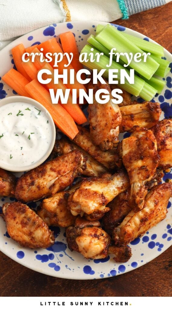 a blue and white spotted plate holding seasoned air fryer chicken wings with a side of ranch, carrot sticks, and celery sticks. Text overlay says "crispy air fryer chicken wings"