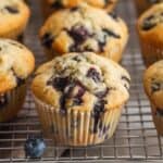 baked blueberry muffins cooling on a wire rack. Fresh berries are on the counter in front of the muffins.