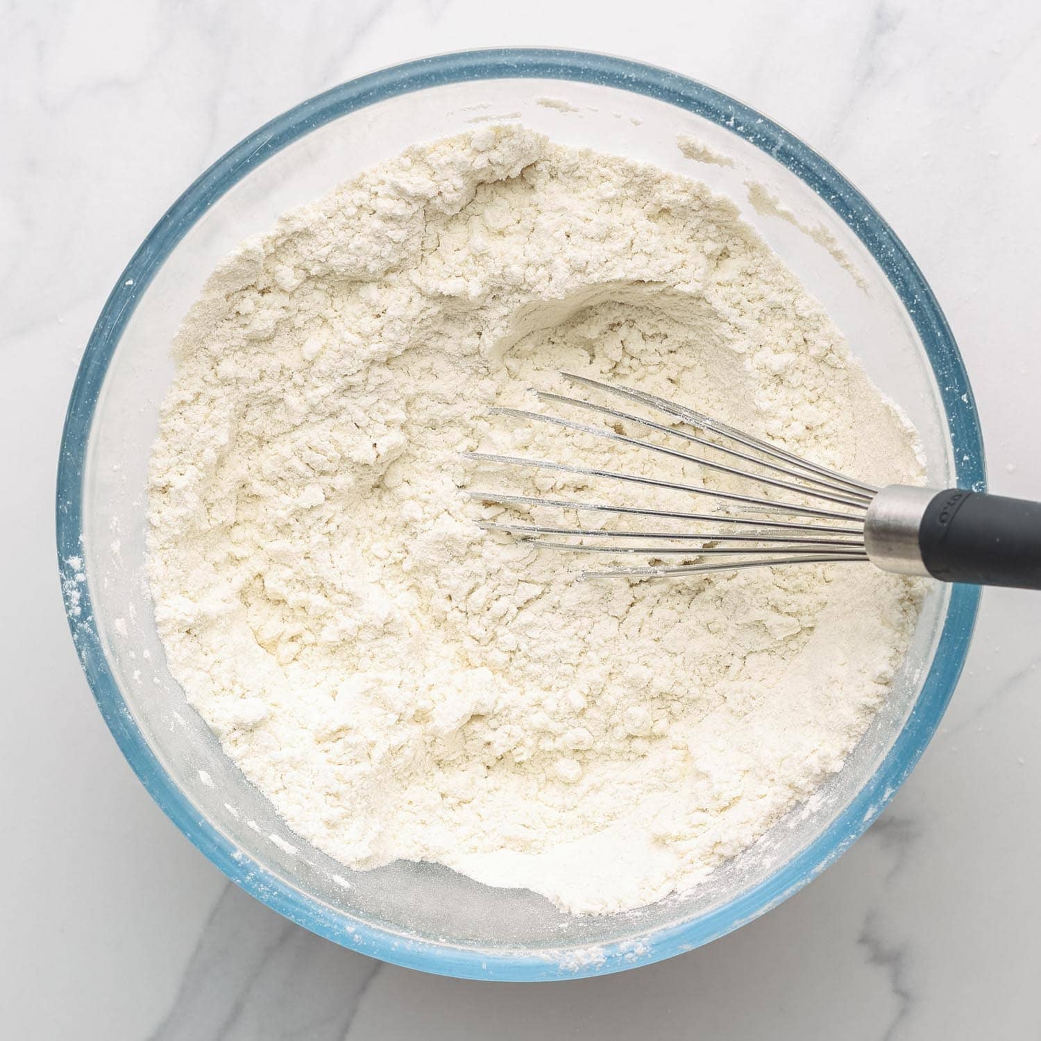 Flour stirred with a whisk in a glass mixing bowl.