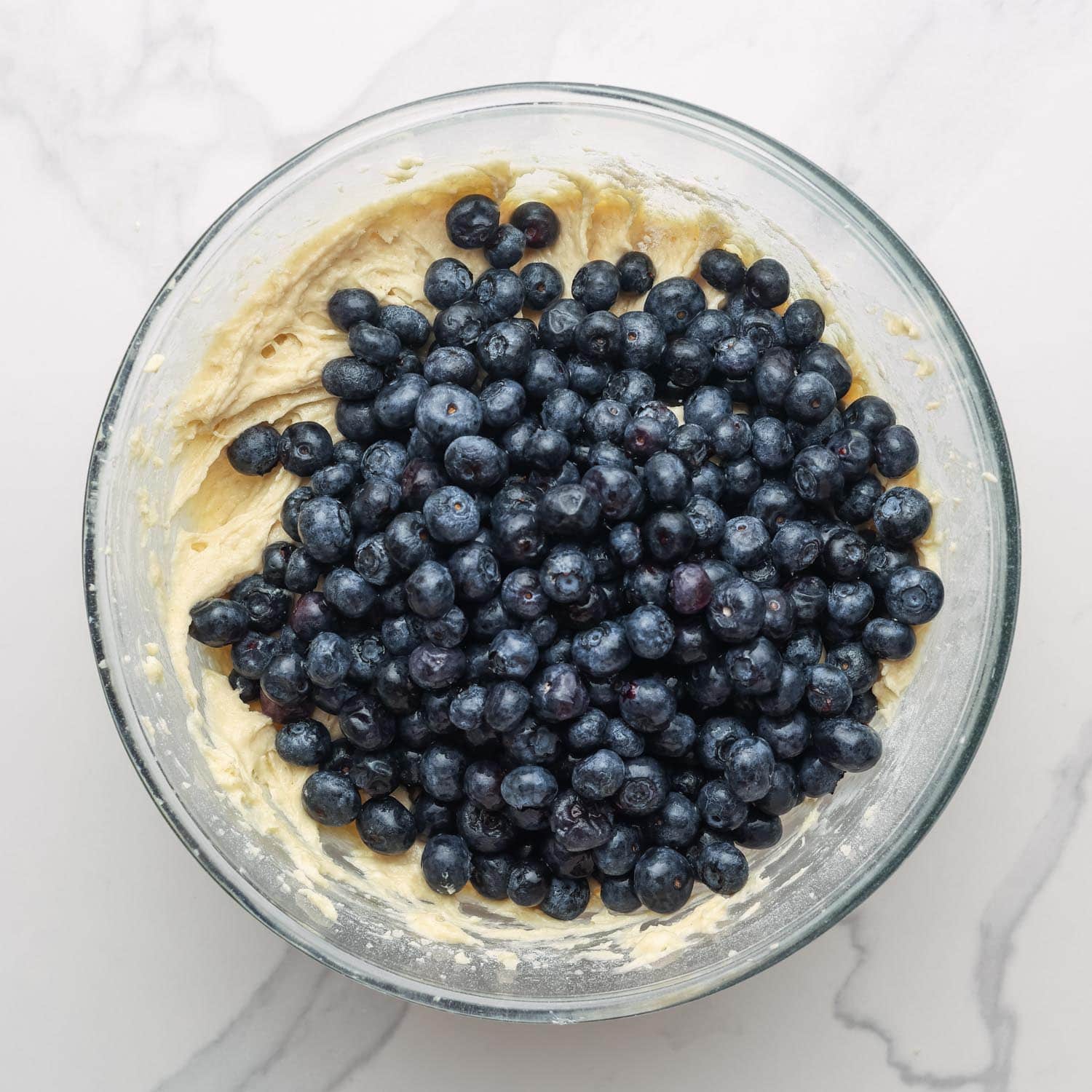 fresh blueberries added to a bowl of muffin batter.