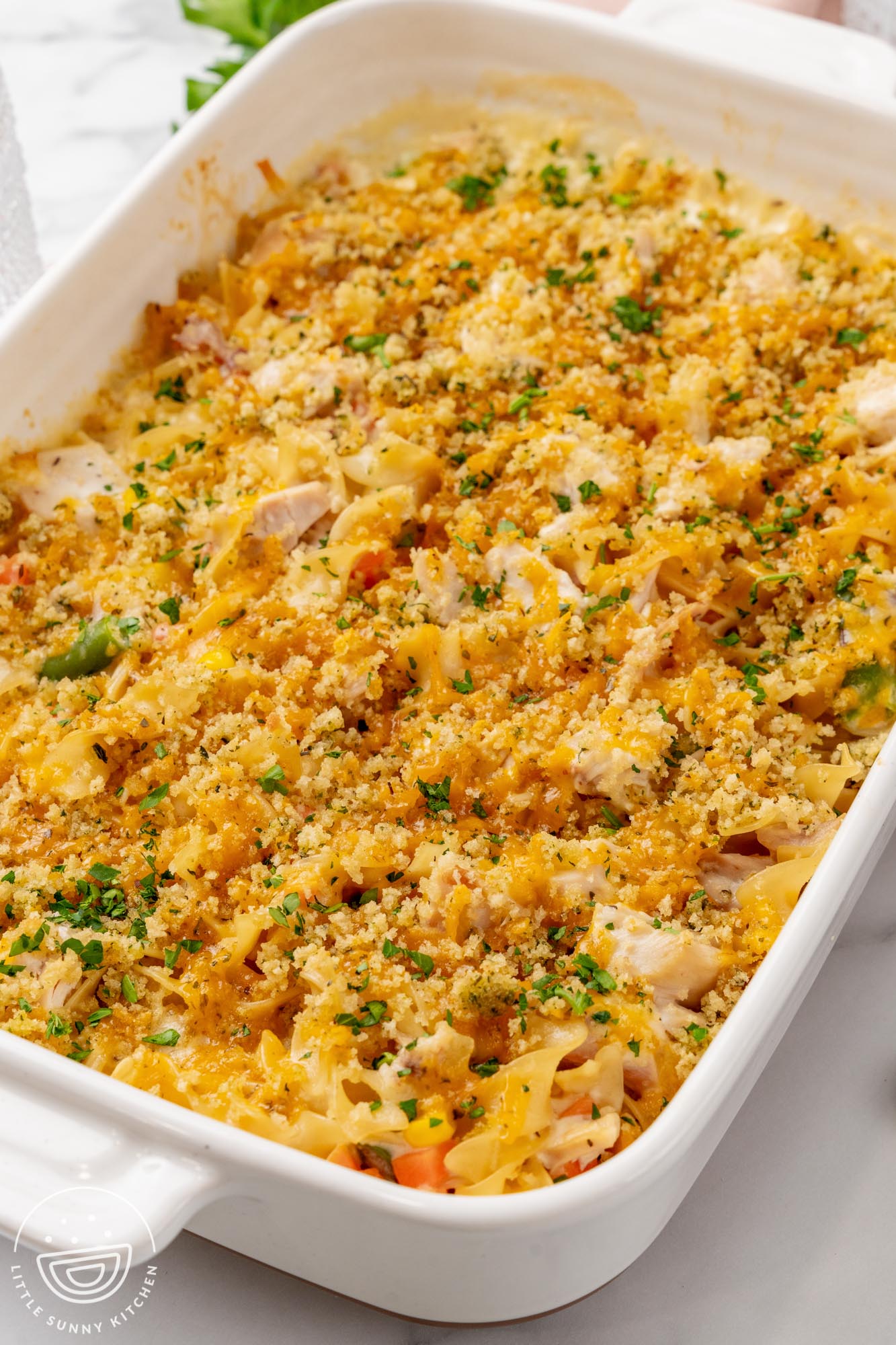 easy chicken noodle casserole in a white baking dish, topped with cheese, breadcrumbs, and chopped parsley to garnish.