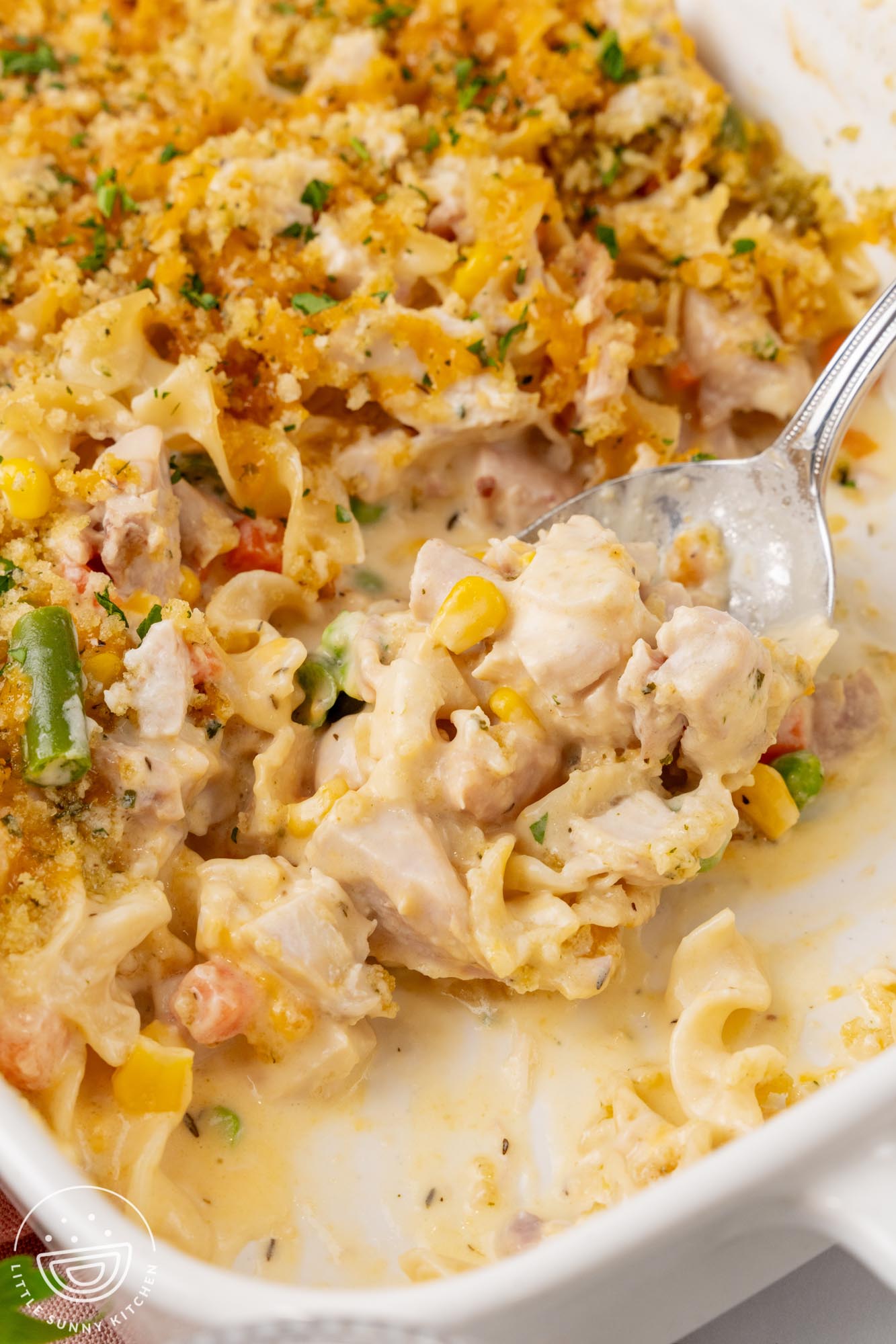 a pan of chicken noodle casserole topped with breadcrumbs. A spoon has removed some servings.