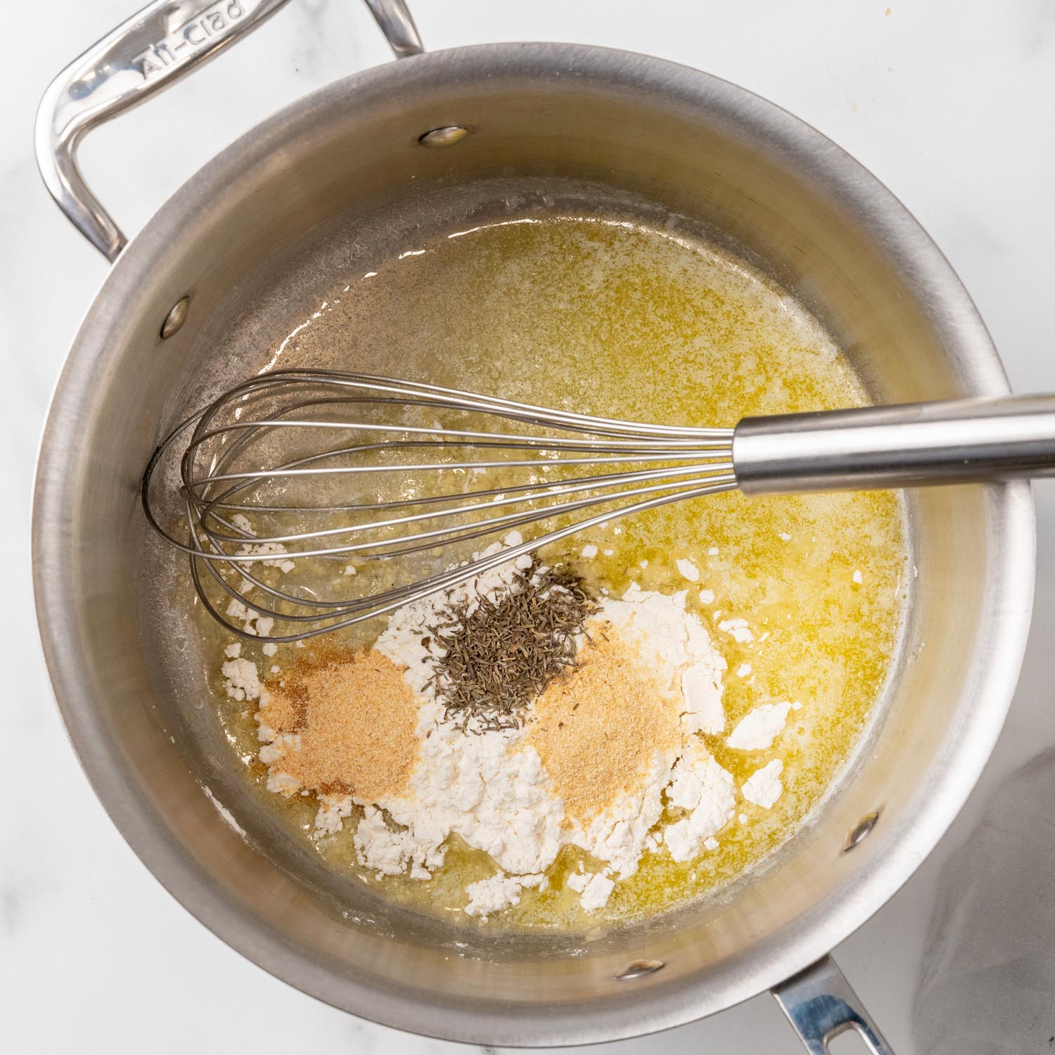 melted butter in a saucepan with flour and seasons to make sauce for chicken noodle casserole. A whisk is about to mix everything together.