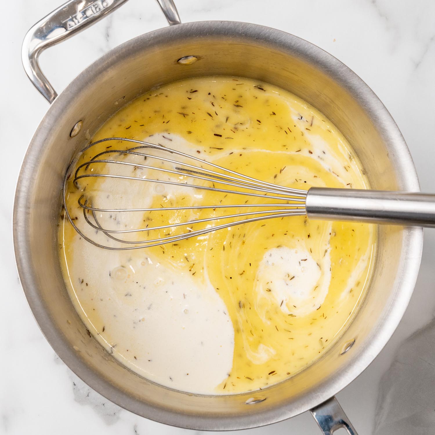 heavy cream added to butter and seasonings to make a creamy sauce for chicken noodle casserole. The mixture is stirred with a metal whisk.