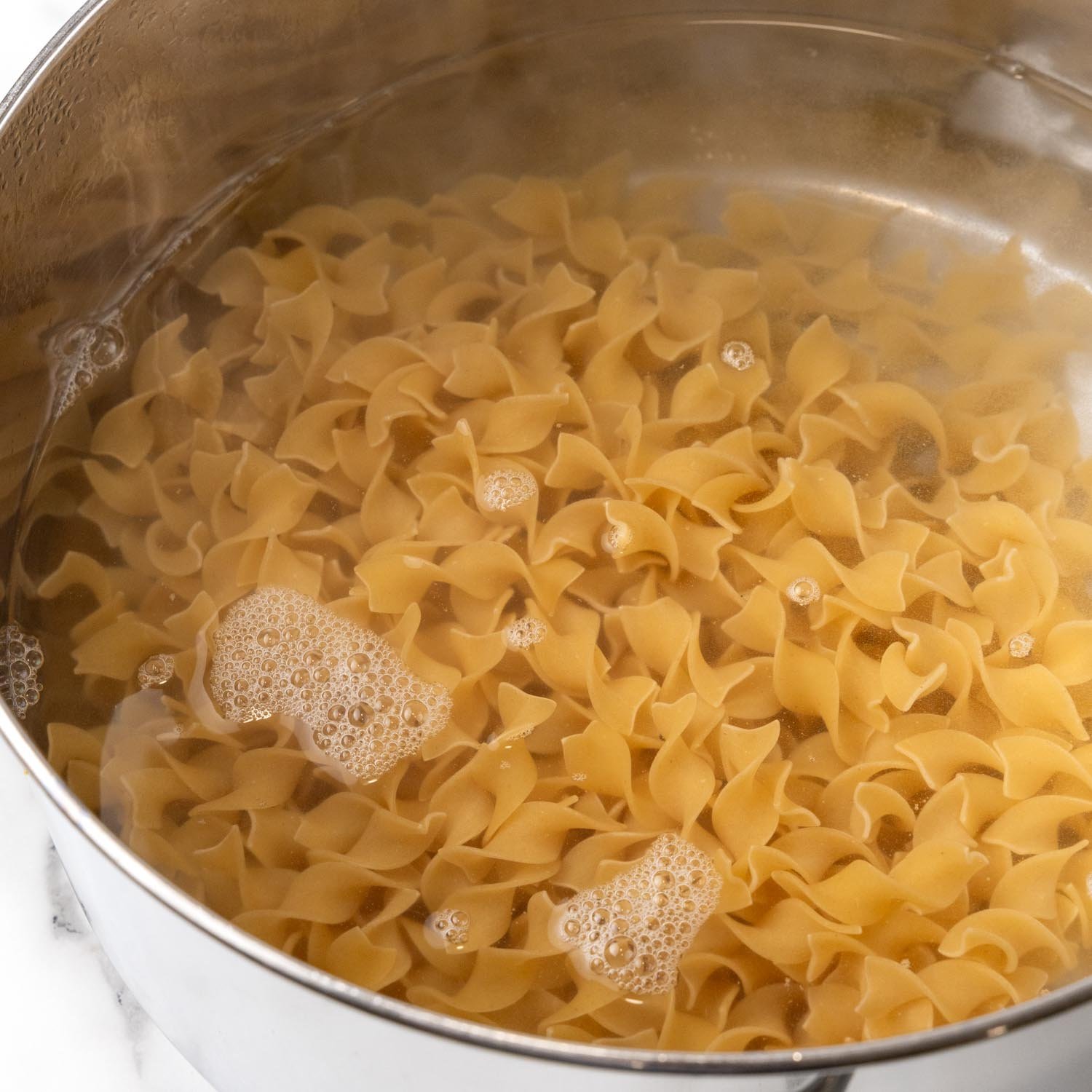 wide egg noodles cooking in boiling water.