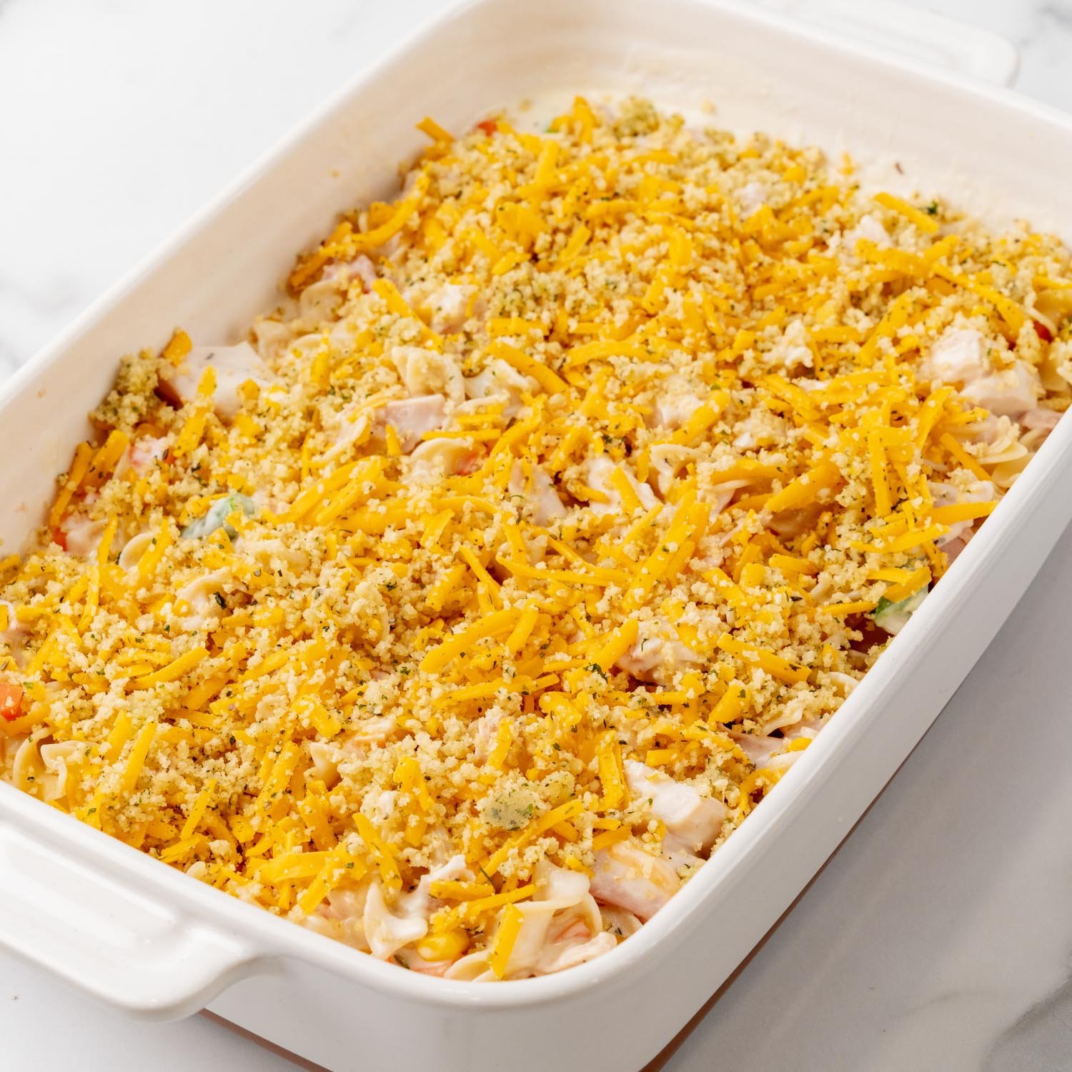 Shredded cheese and seasoned breadcrumbs added to the top of a noodle casserole with chicken.