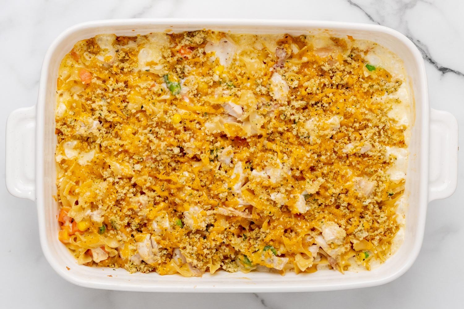 baked chicken noodle casserole in a white 9x13 baking dish, viewed from above to show the melty cheese and breadcrumbs on top.