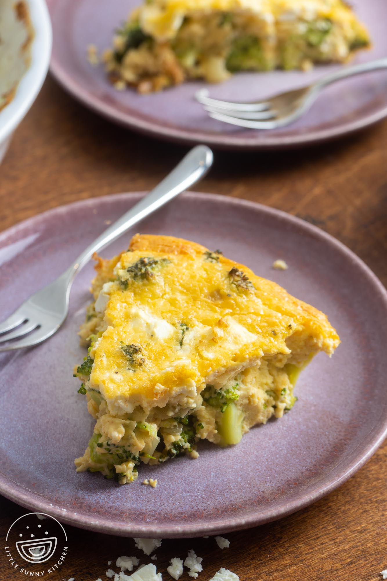 a wedge slice of crustless broccoli quiche on a purple ceramic plate with a small three-tined fork.