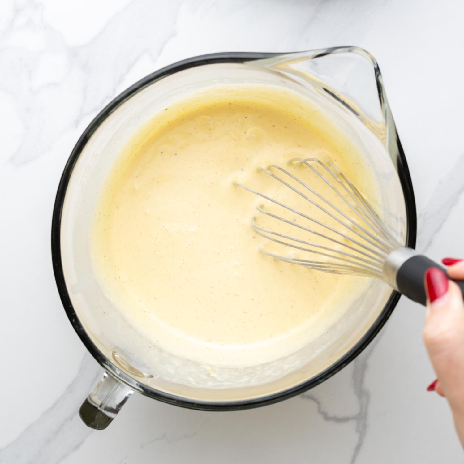 Cream and egg mixture for quiche whisked in a glass mixing bowl.