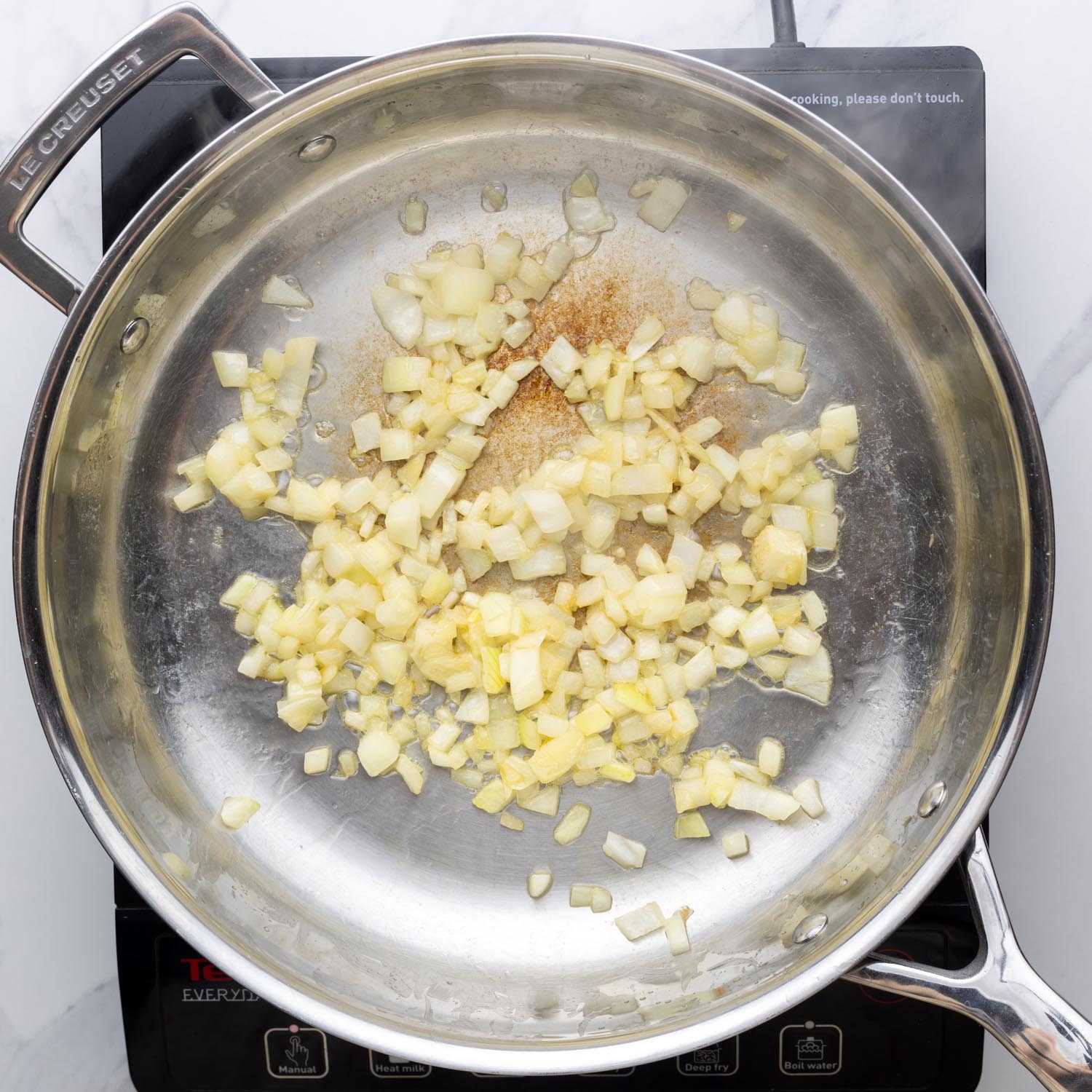 diced onions sauteeing in a metal skillet.