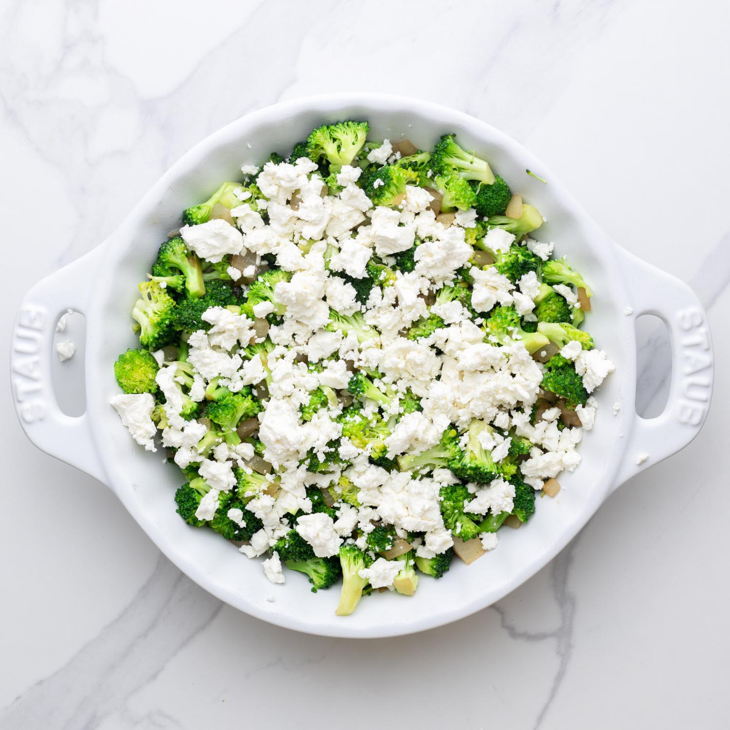 broccoli, onions, and feta cheese arranged in a pie plate for crustless quiche.