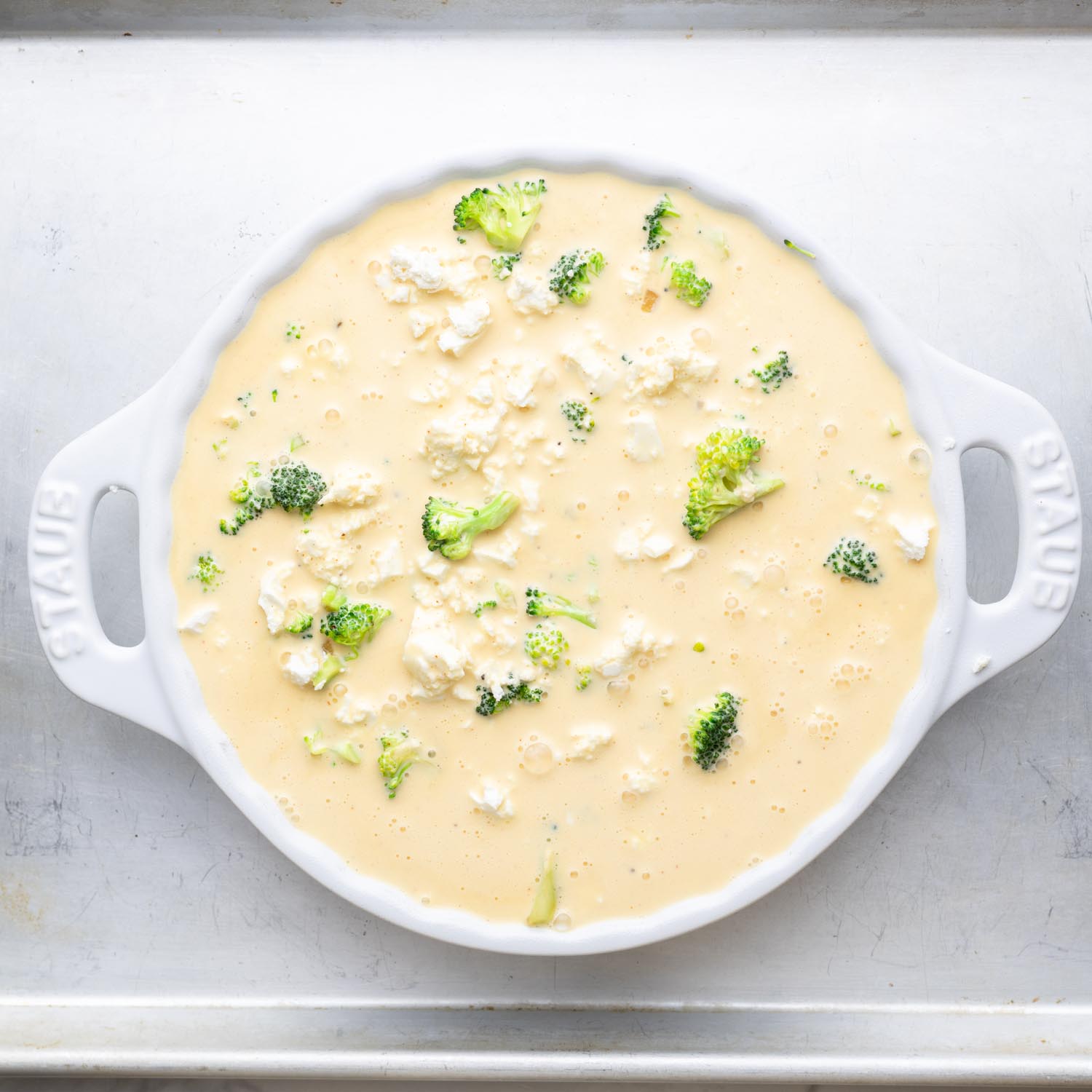 Egg and cream mixture for quiche poured over broccoli and cheese in a white ceramic pie plate.