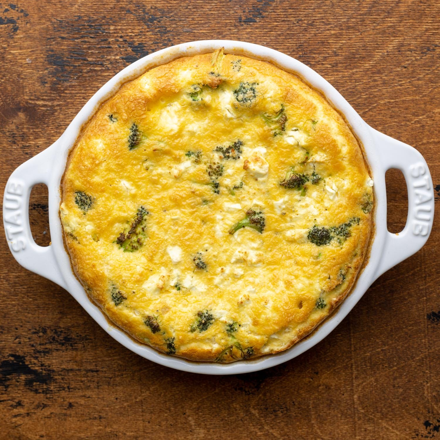 Baked crustless broccoli quiche in a white ceramic pie plate. The quiche is browned on the edges and on top.