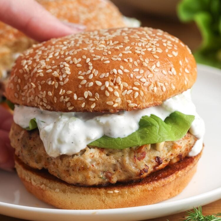 a greek chicken burger topped with lettuce and tzatziki sauce on a sesame seed bun.