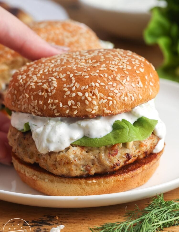 a greek chicken burger topped with lettuce and tzatziki sauce on a sesame seed bun.