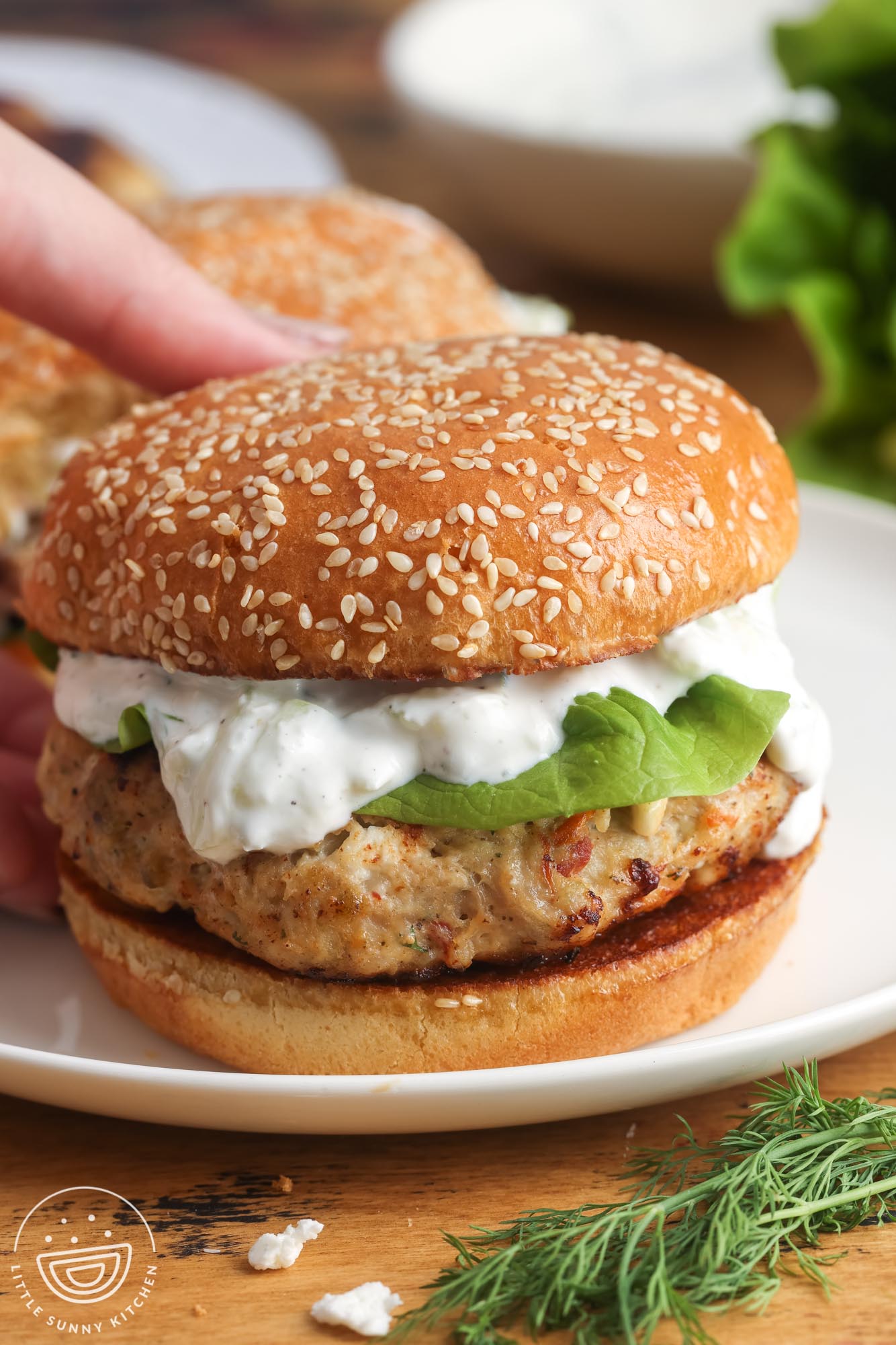 a greek chicken burger topped with lettuce and tzatziki sauce on a sesame seed bun.