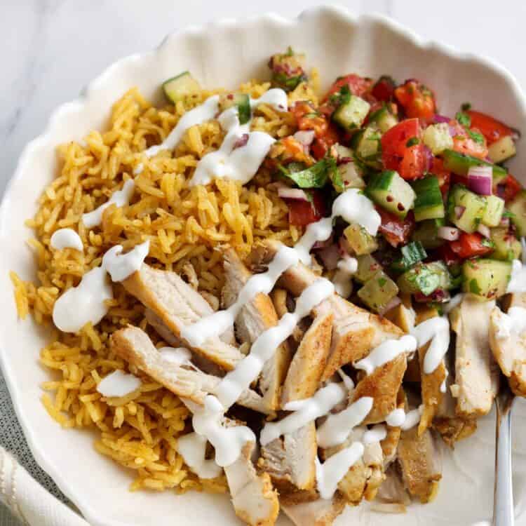 a bowl of shawarma rice with sliced chicken and cucumber shirazi salad, drizzled with yogurt sauce.