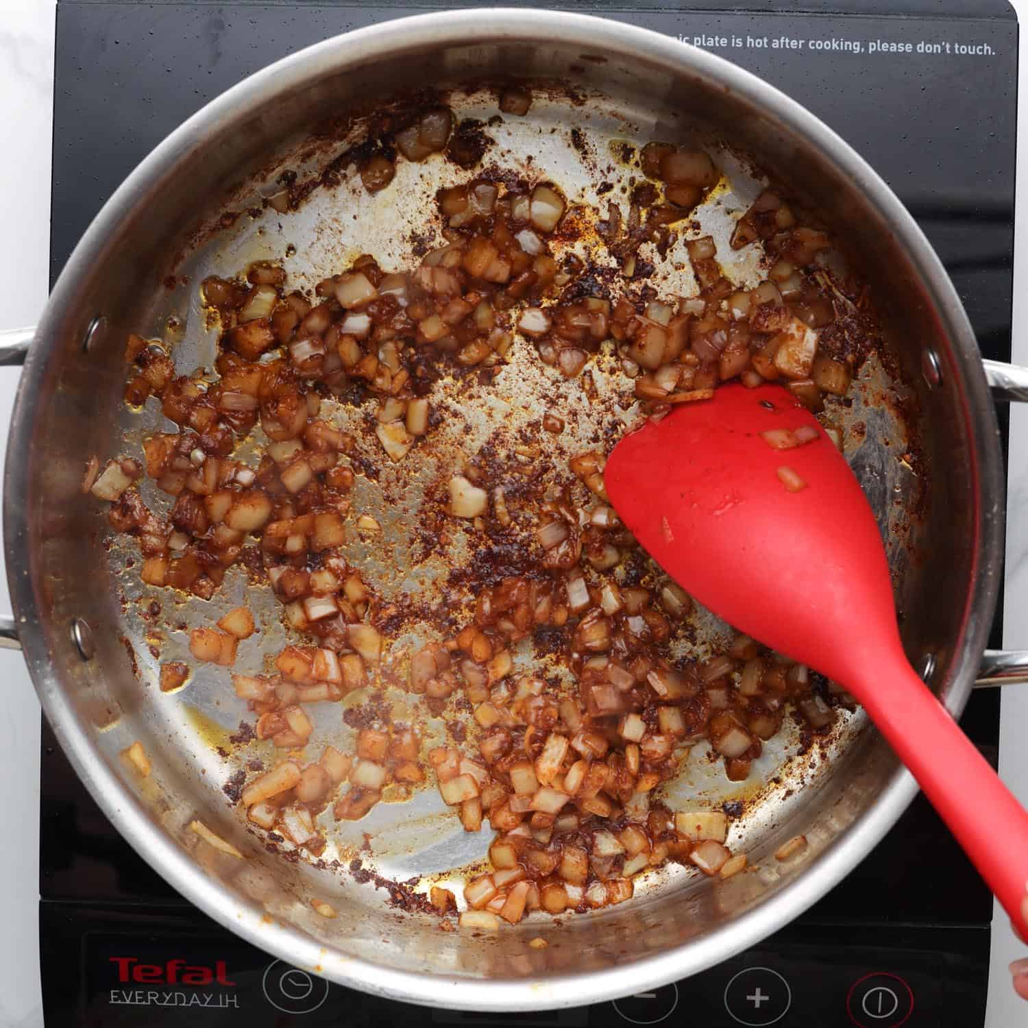 diced yellow onion sauteed in a metal skillet with a red spoon. 