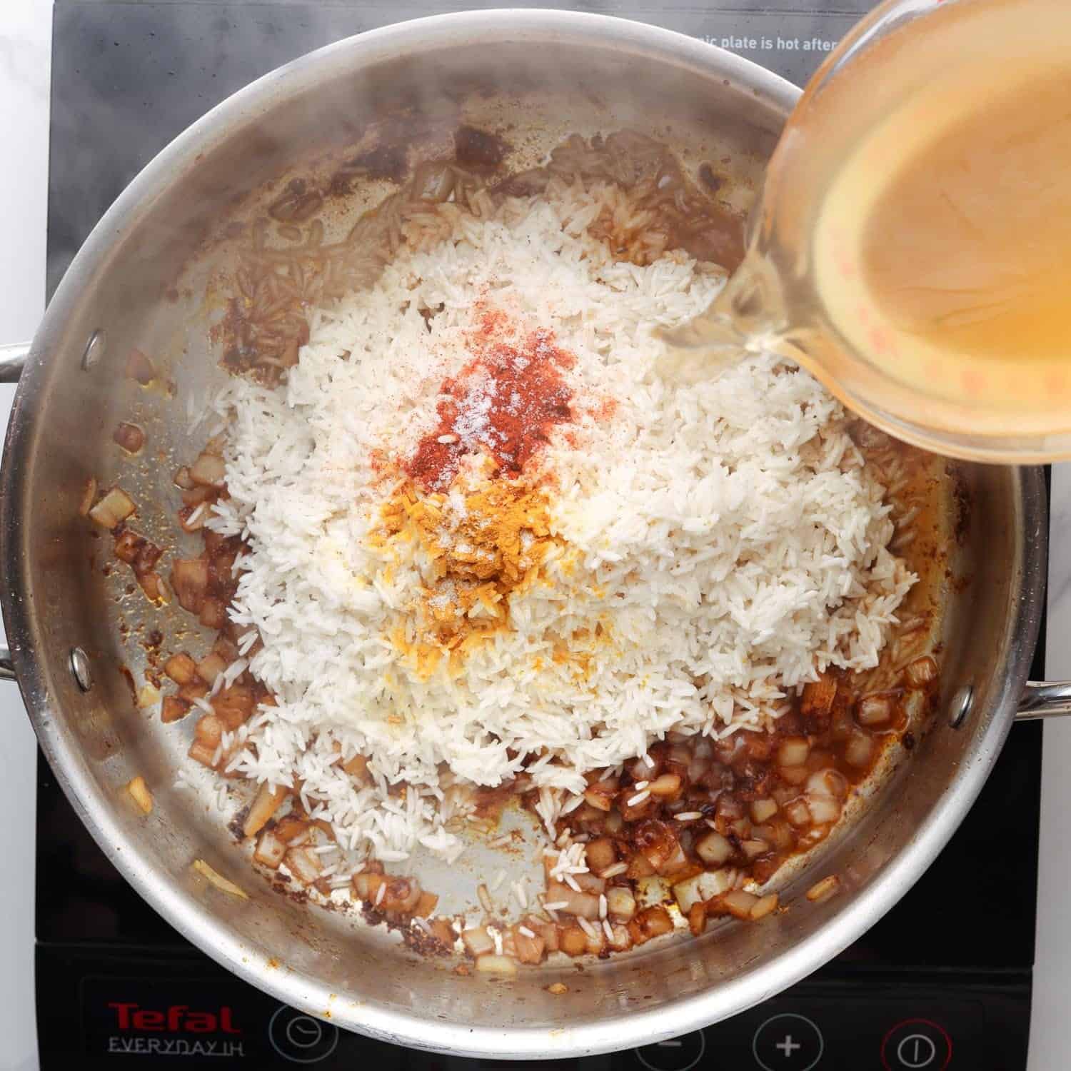 basmati rice, broth, and seasonings added to a skillet with sauteed onions. 