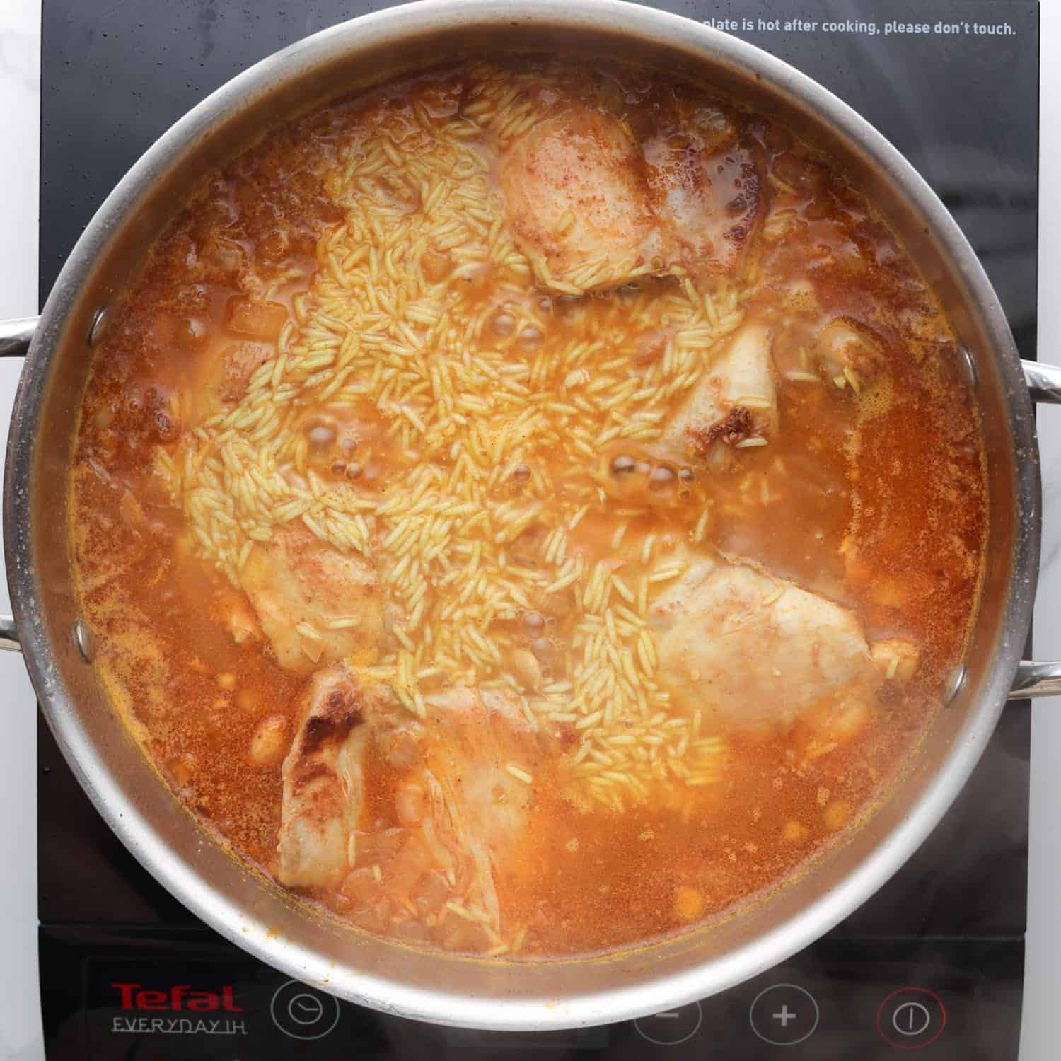 chicken and rice in broth in a metal skillet over an electric heating element. 