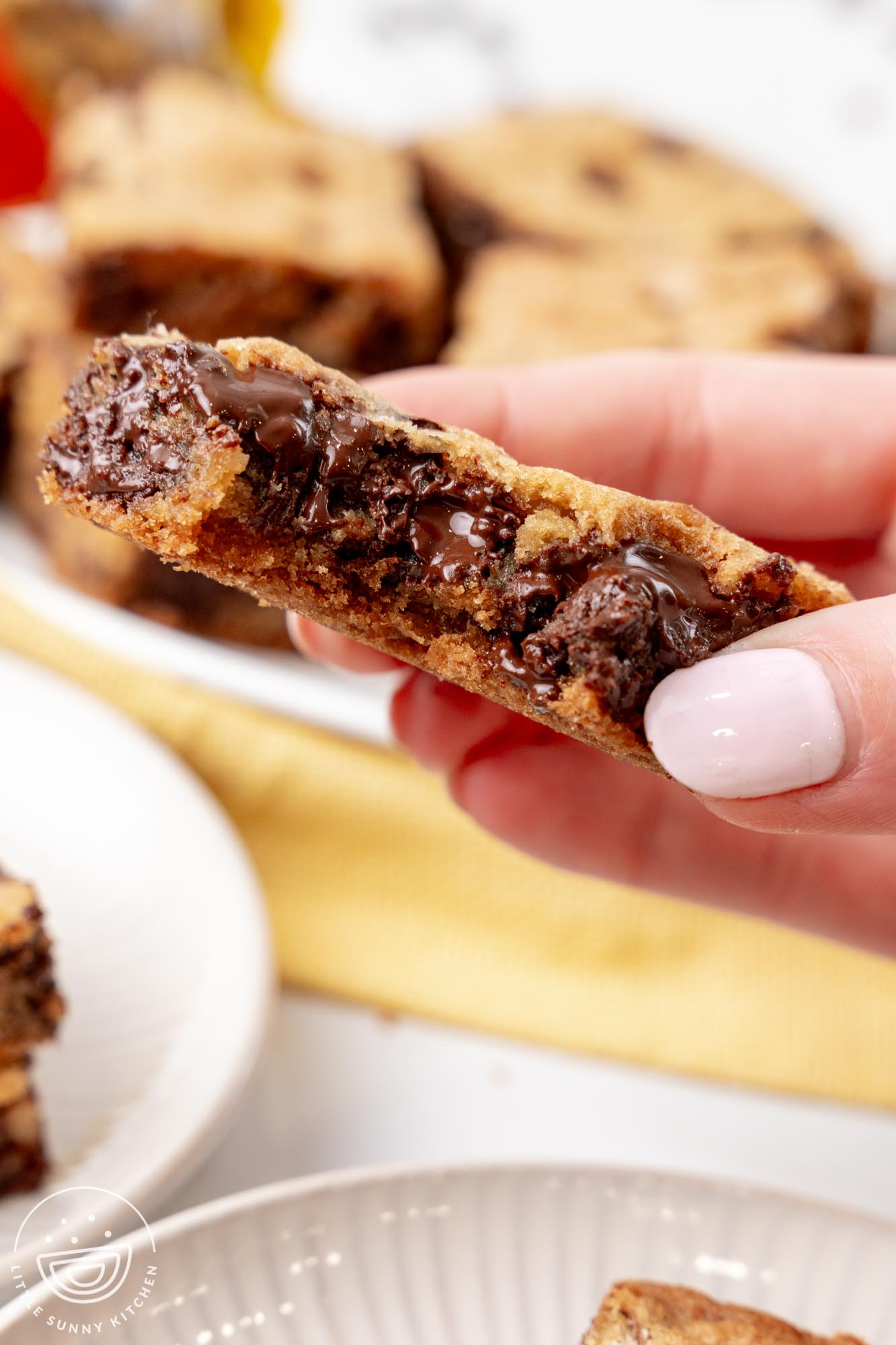 a hand picking up a toll house cookie bar with gooey chocolate chips. A bite has been taken.