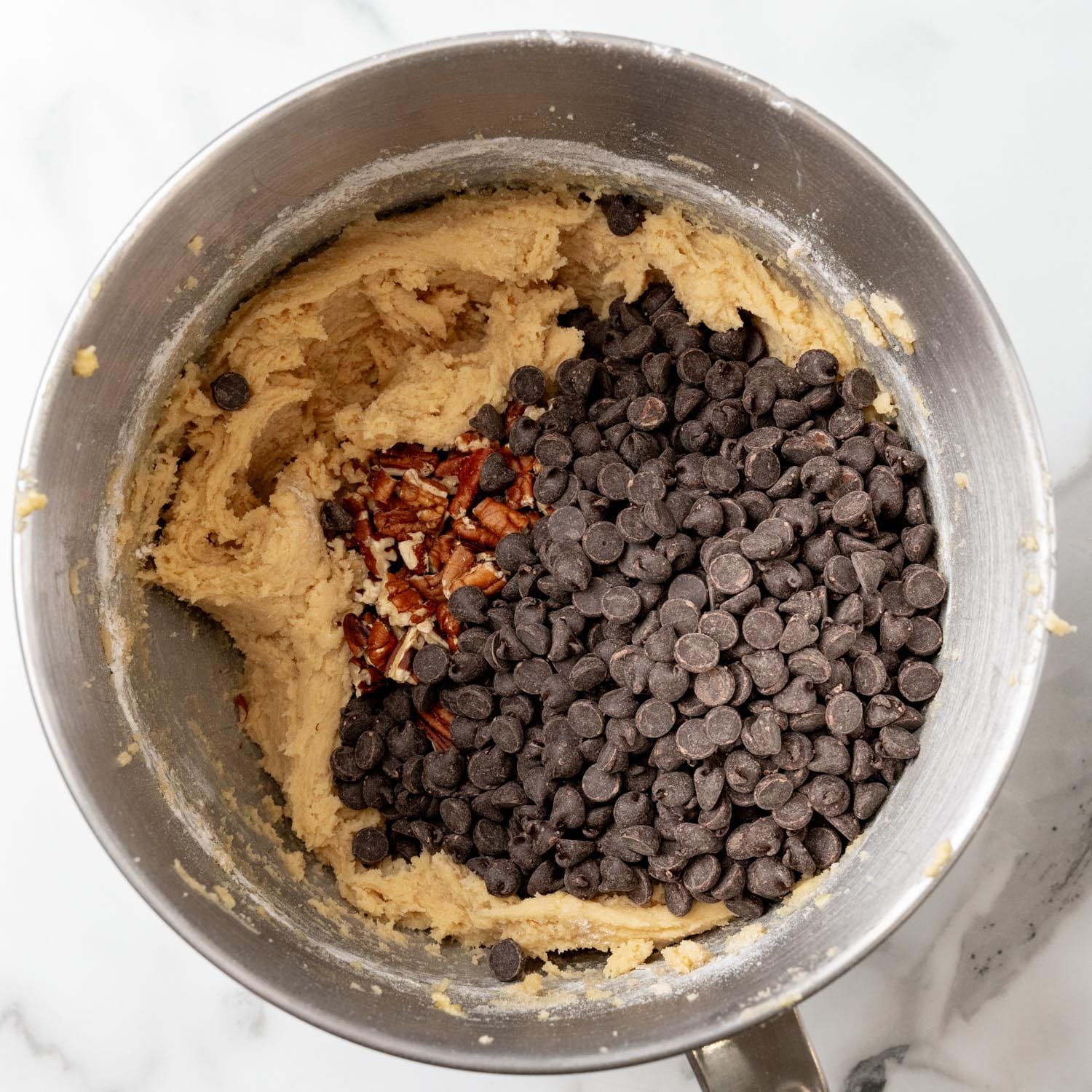 chocolate chips and chopped pecans added to cookie bar dough in a metal mixing bowl.