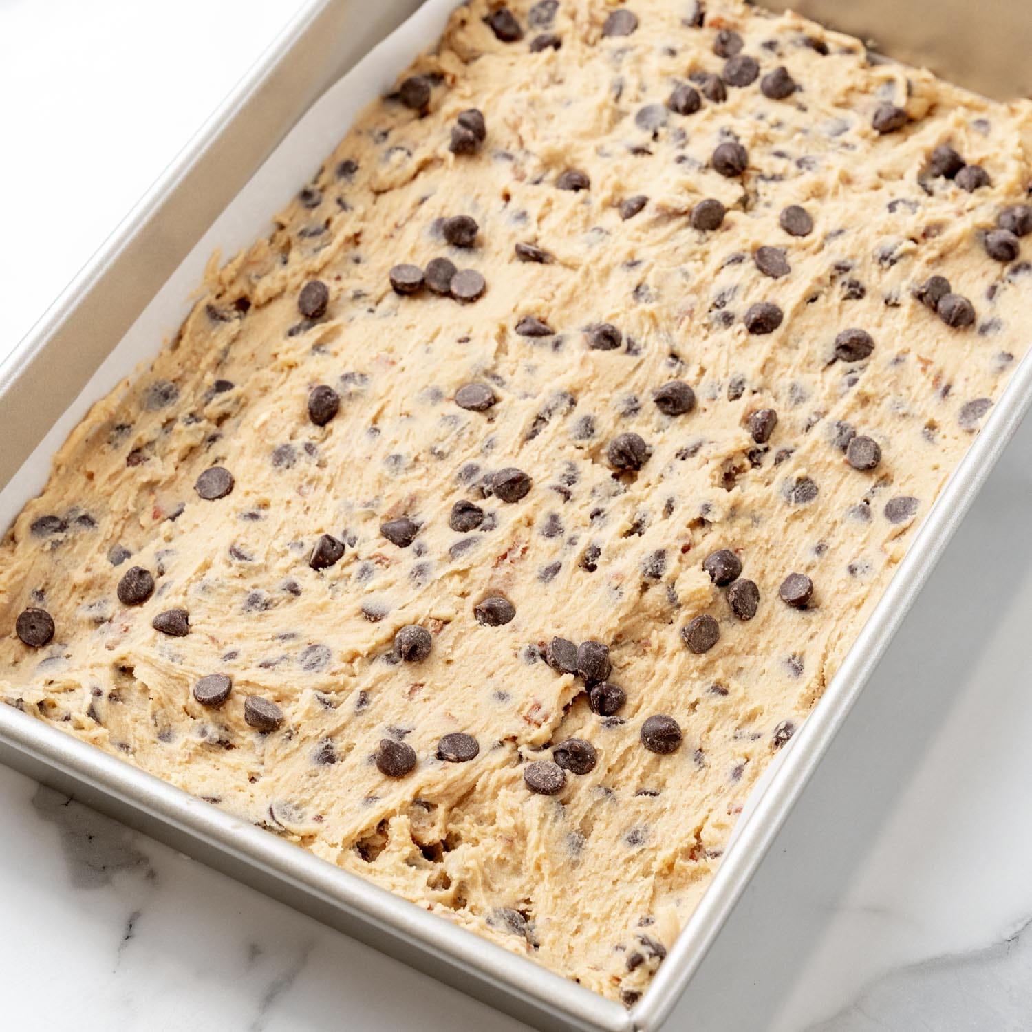 toll house cookie bars dough spread into a parchment-lined 9x13 metal baking pan.