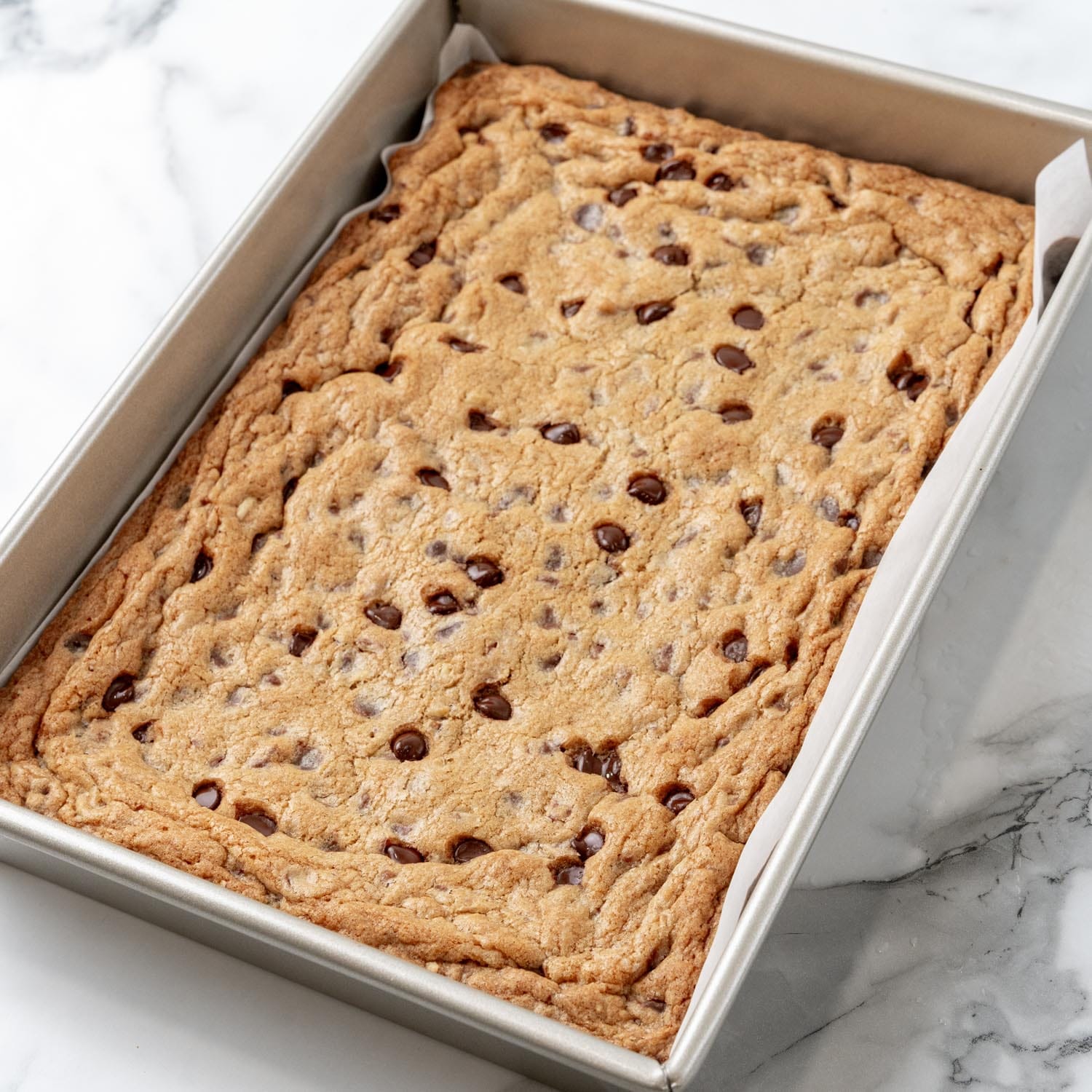 baked toll house cookie bars in a metal baking pan. The top is crackled and golden brown.