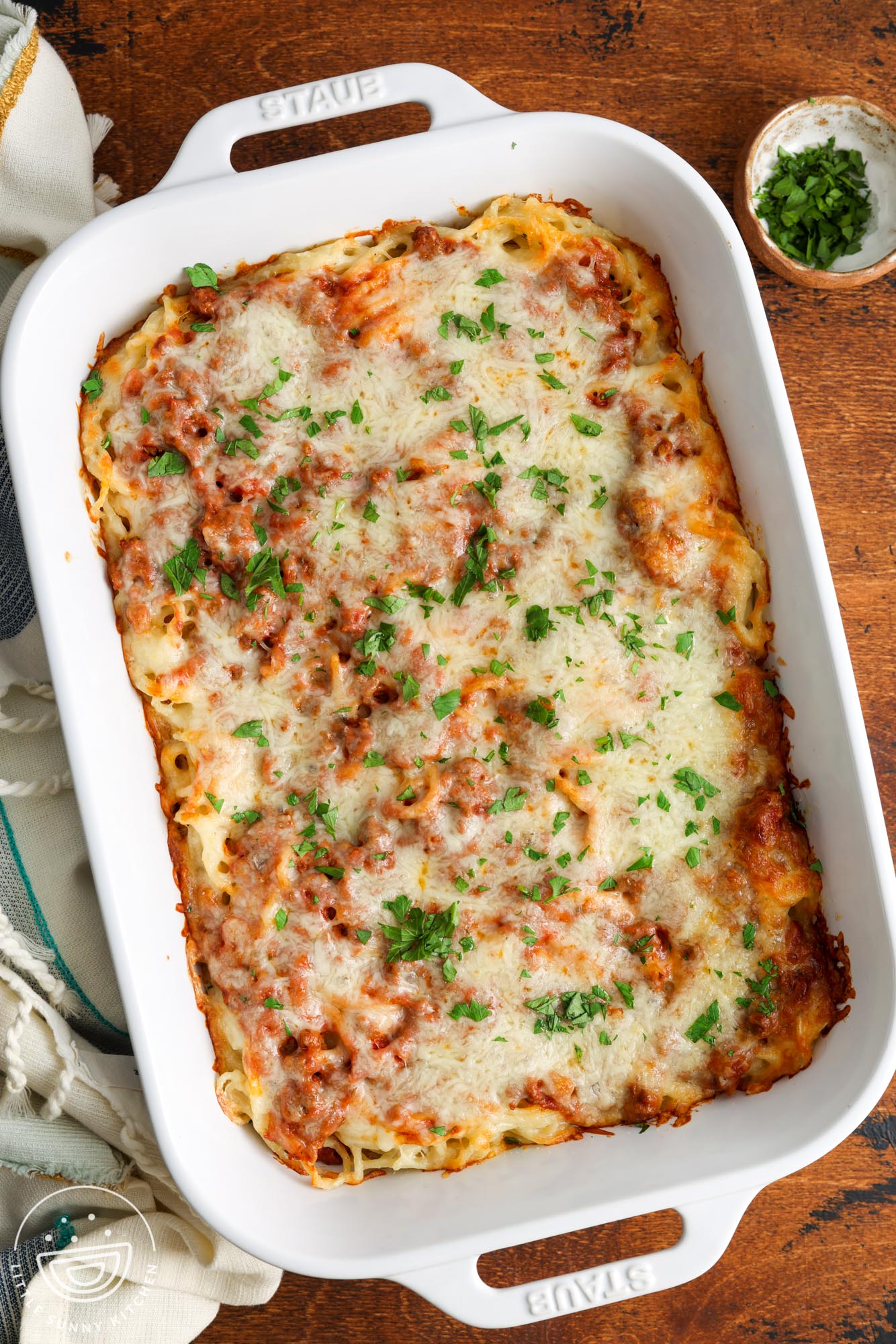 a white casserole dish of baked cream cheese spaghetti on a wooden table.