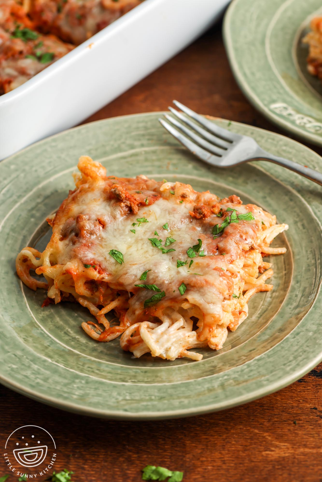 a square piece of baked cream cheese spaghetti on a green ceramic plate with a fork.