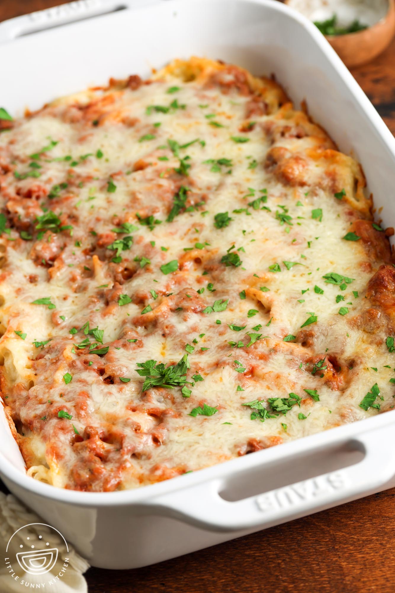 cream cheese spaghetti baked in a white casserole dish that is set on a wooden table.