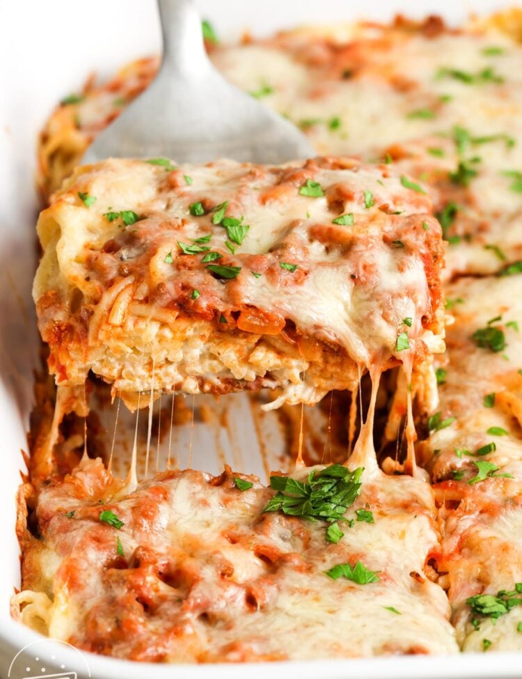 a spatula lifting up a square piece of cream cheese spaghetti casserole.