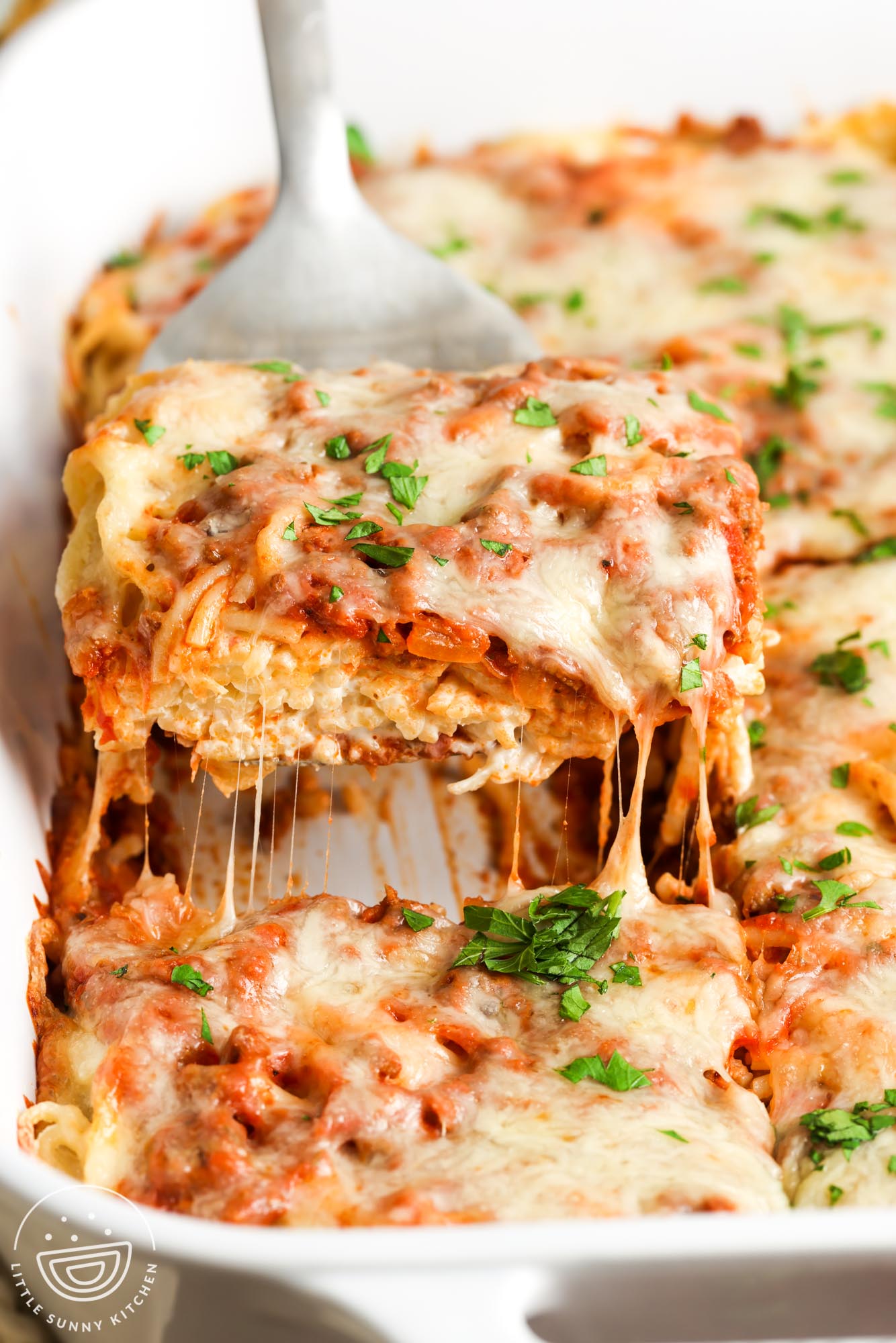 a spatula lifting up a square piece of cream cheese spaghetti casserole.