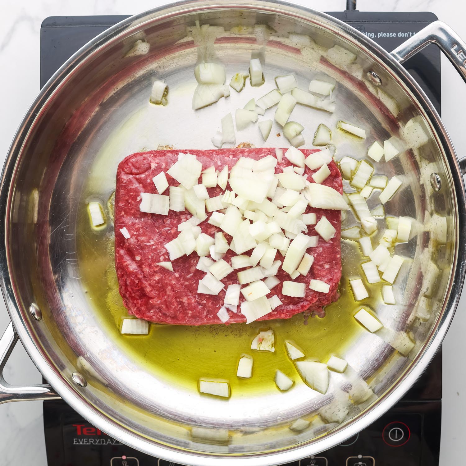 ground beef and diced onions in a stainless steel skillet with olive oil.