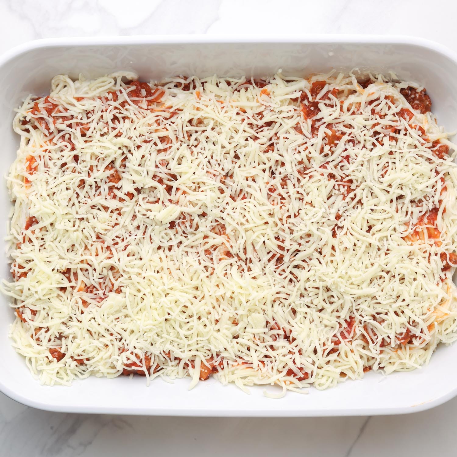 shredded mozzarella cheese added cream cheese spaghetti casserole in a white ceramic baking dish.