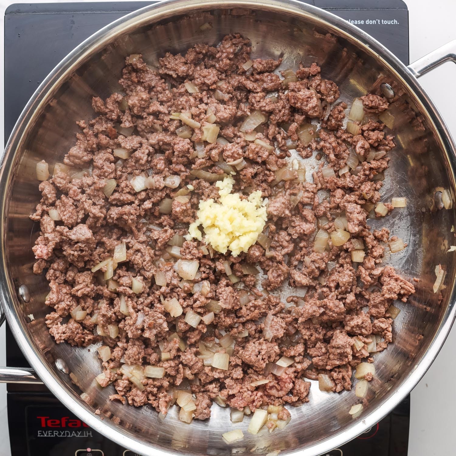 cooked ground beef and onion in a pan. minced garlic is added.