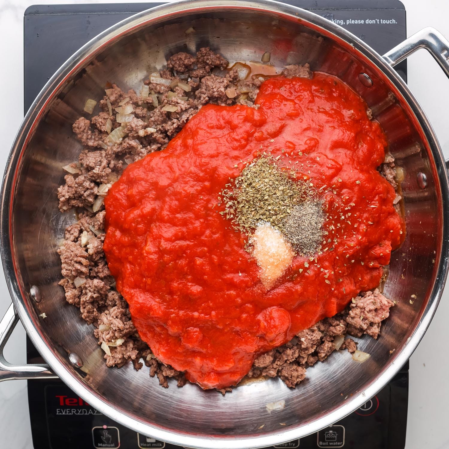 tomato sauce and seasonings added to cooked ground beef in a skillet.