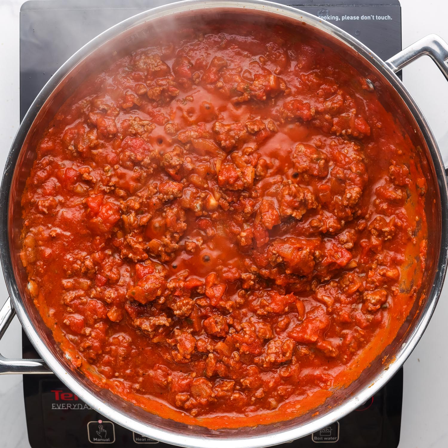 beef tomato sauce cooking in a stainless steel pan over an electric burner.