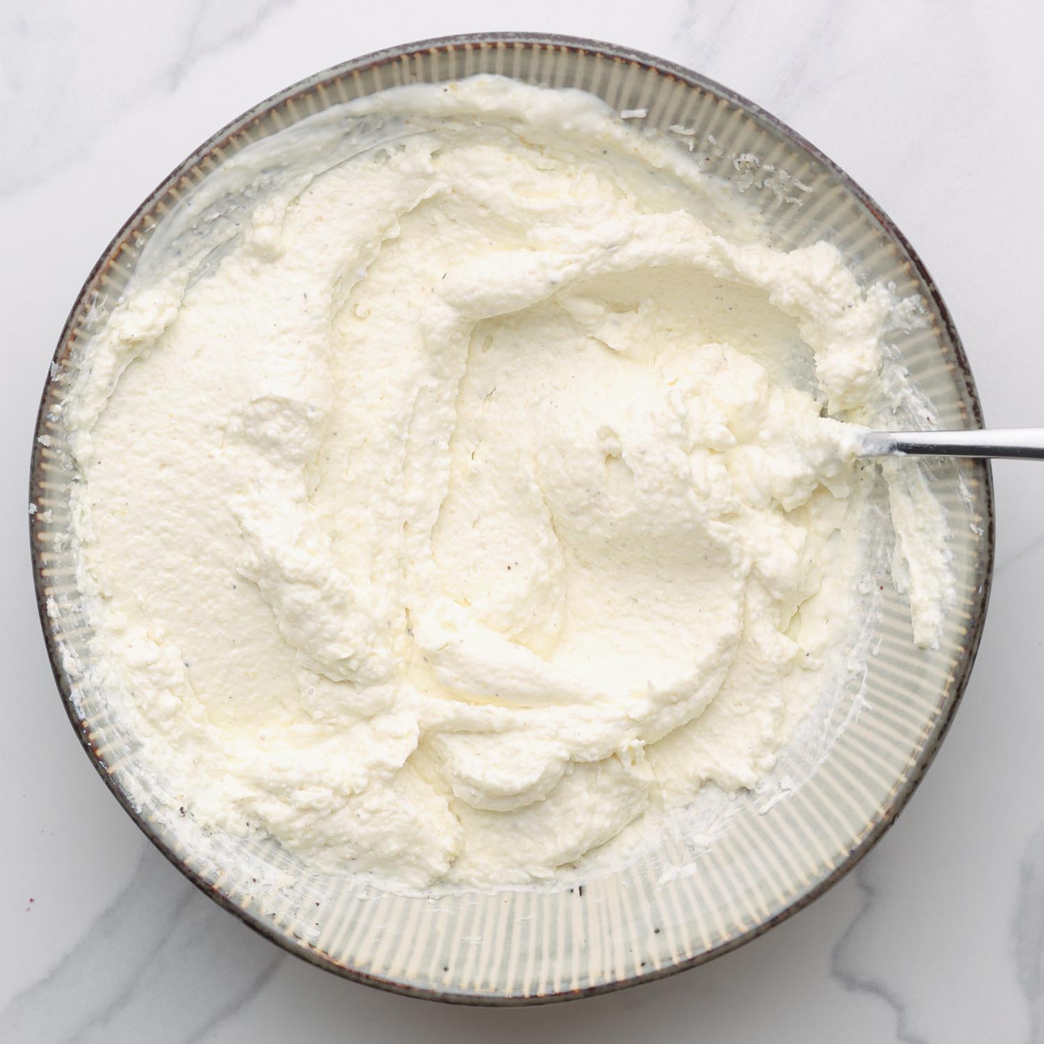 softened cream cheese mixed with sour cream and parmesan cheese in a ceramic bowl.