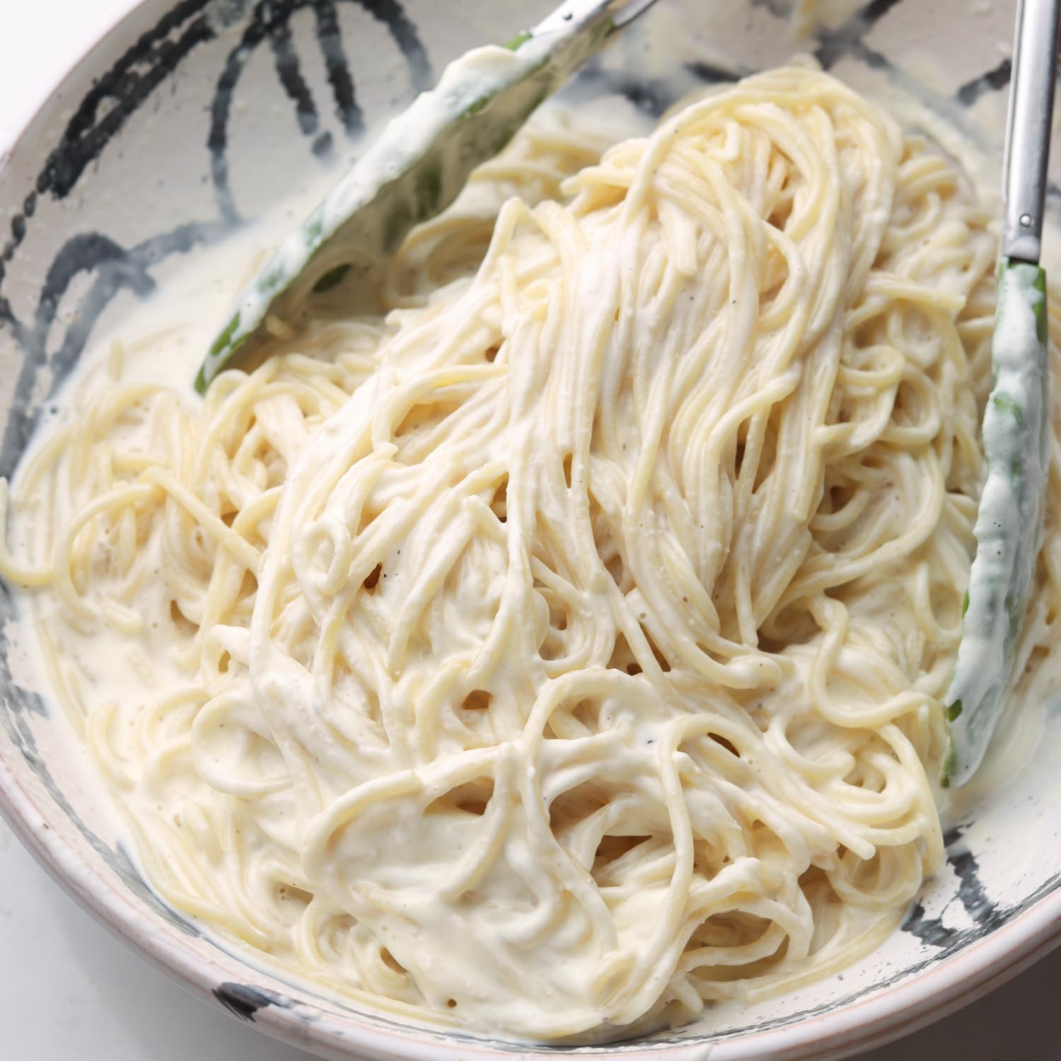 cooked spaghetti tossed with cream cheese sauce in a bowl.