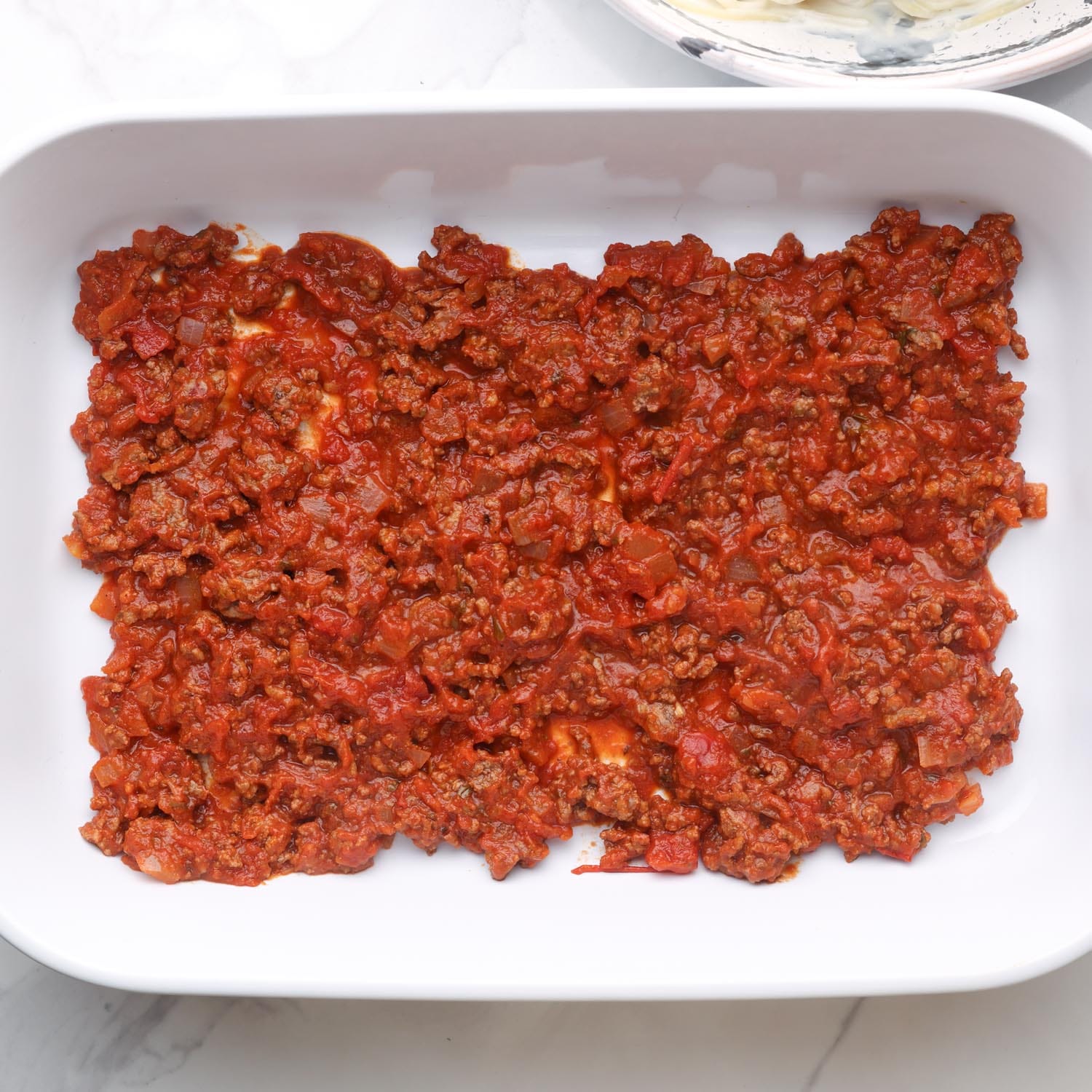 meatsauce in the bottom of a white rectangular casserole dish.