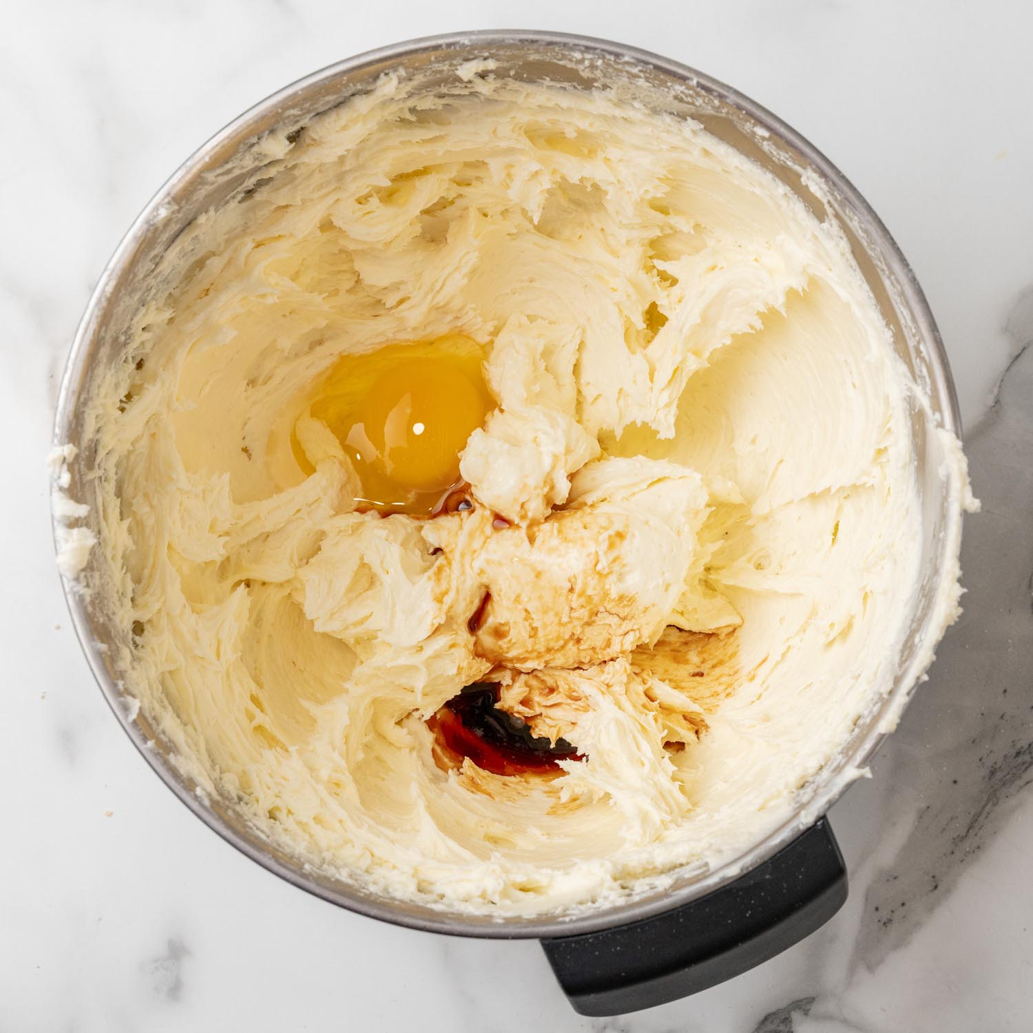 whipped cream cheese in a mixing bowl with an egg and vanilla added.