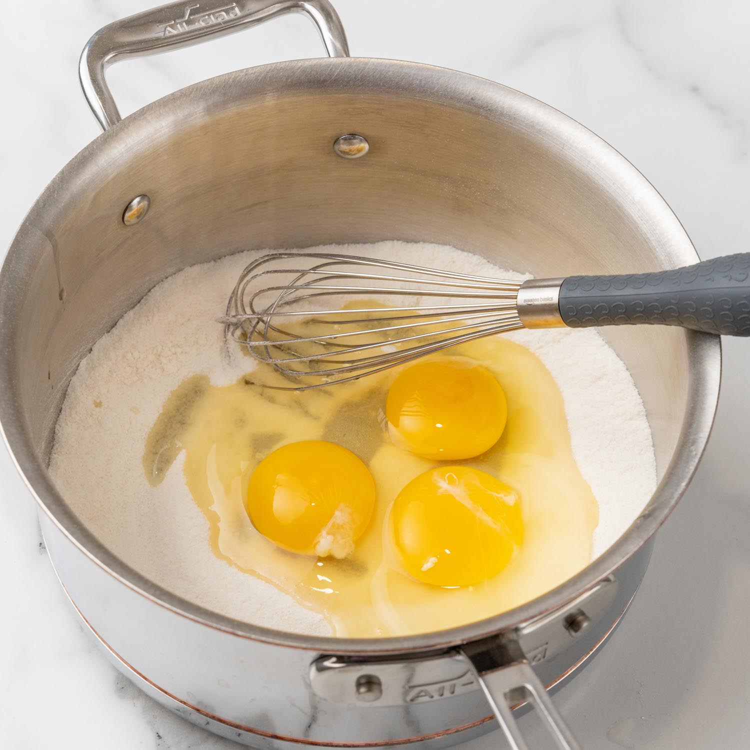 Three eggs added to flour and sugar in a metal saucepan.